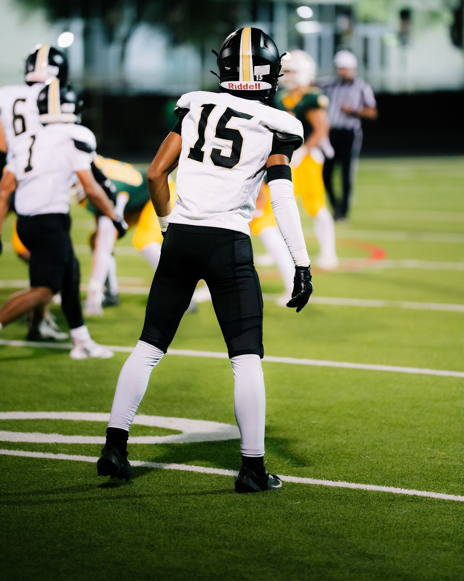 Football player wearing number 15 black and white uniform stands on field during night game.