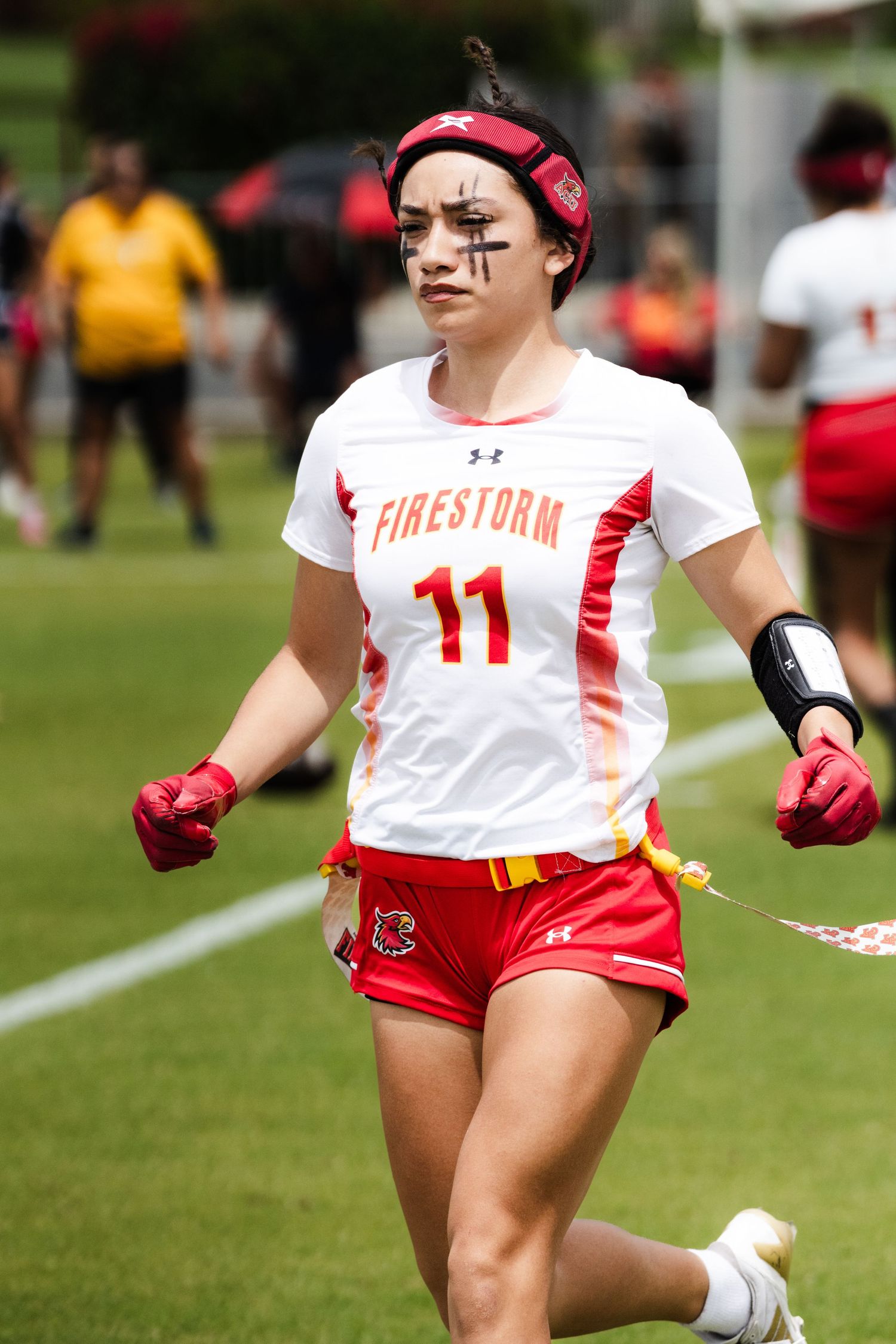 Firestorm #11 female lacrosse player with eye black running on field in red and white uniform.