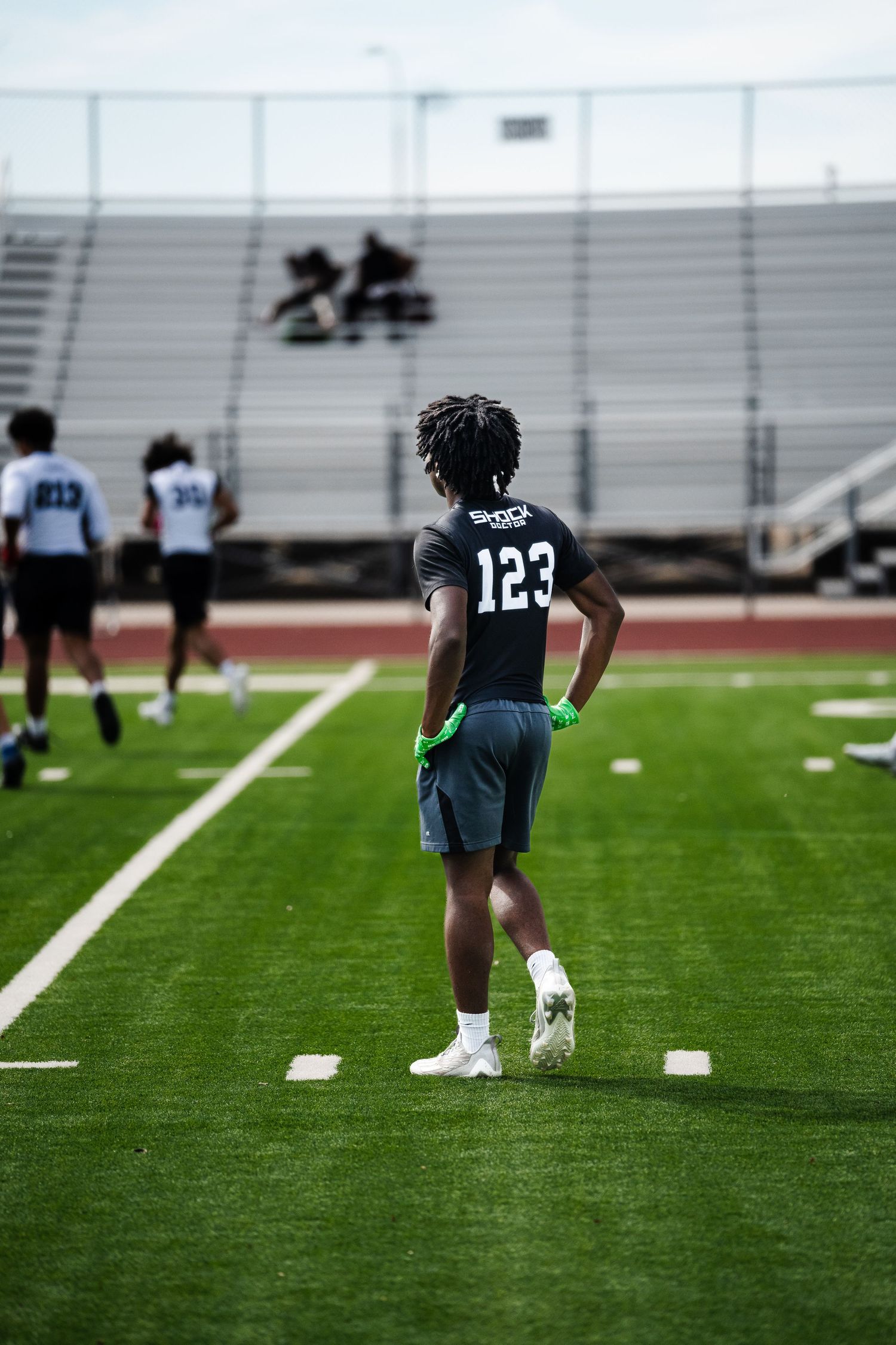 Football player wearing number 123 Shock Doctor jersey standing on green turf field during combine.