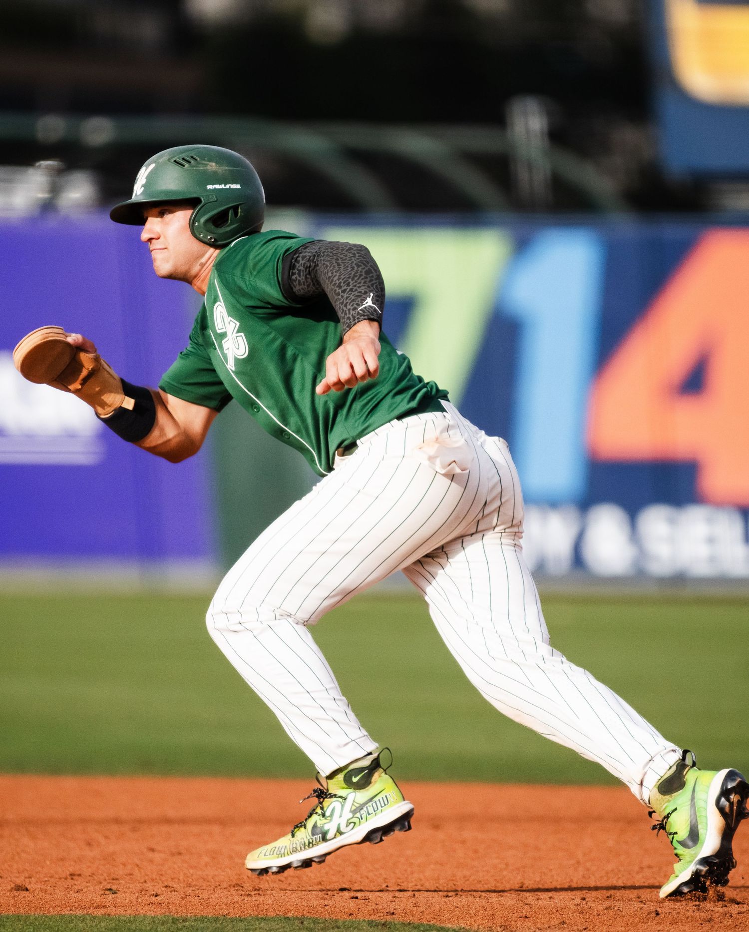 Hawaii baseball player in green uniform runs the bases during a competitive game.