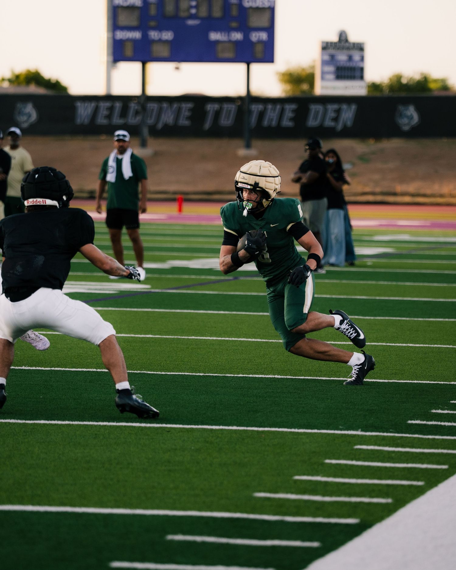 Football player in green uniform runs with the ball during a game at Welcome to the Den stadium.