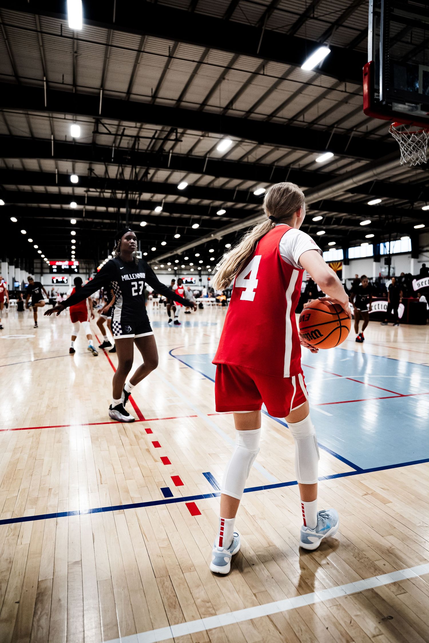 Female basketball player in red uniform holds ball on court during indoor basketball tournament.