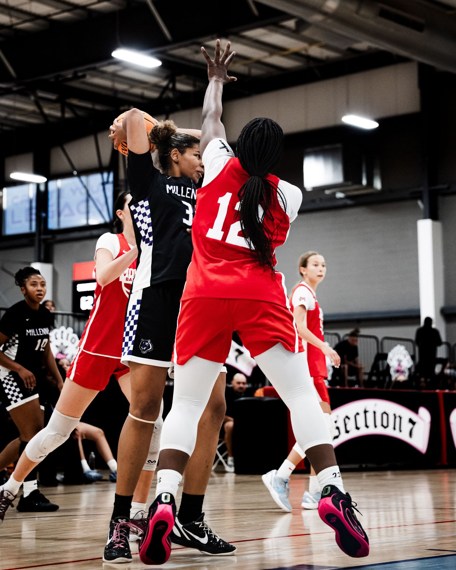 Female basketball player in black Millennia uniform attempts shot against red-uniformed defender.