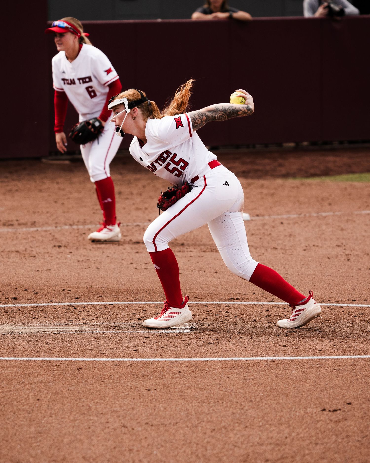 Texas Tech softball pitcher in white and red uniform mid-wind-up on the mound during a college softball game.