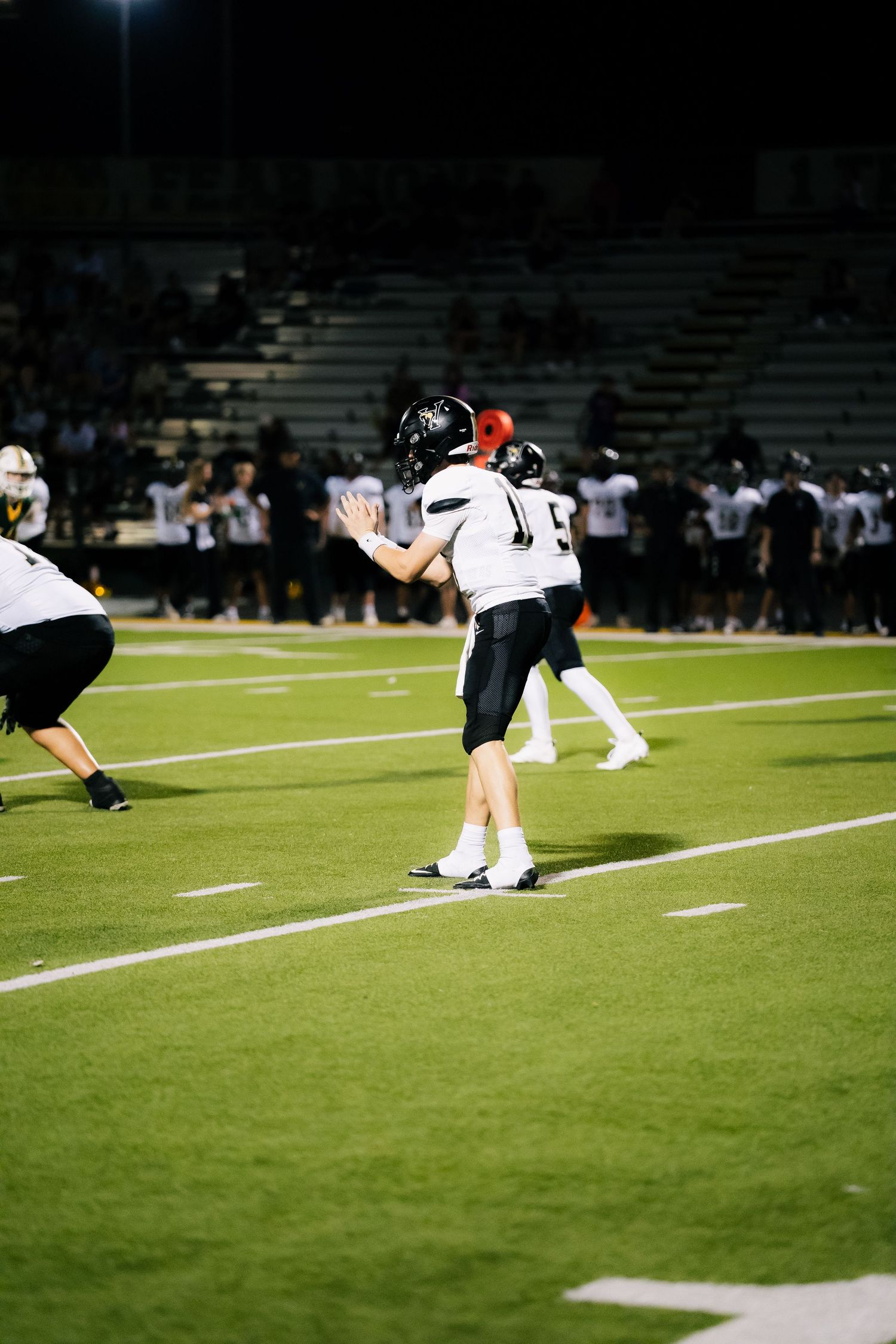 High school football player in white uniform prepares to throw a pass during a night game on a green field.