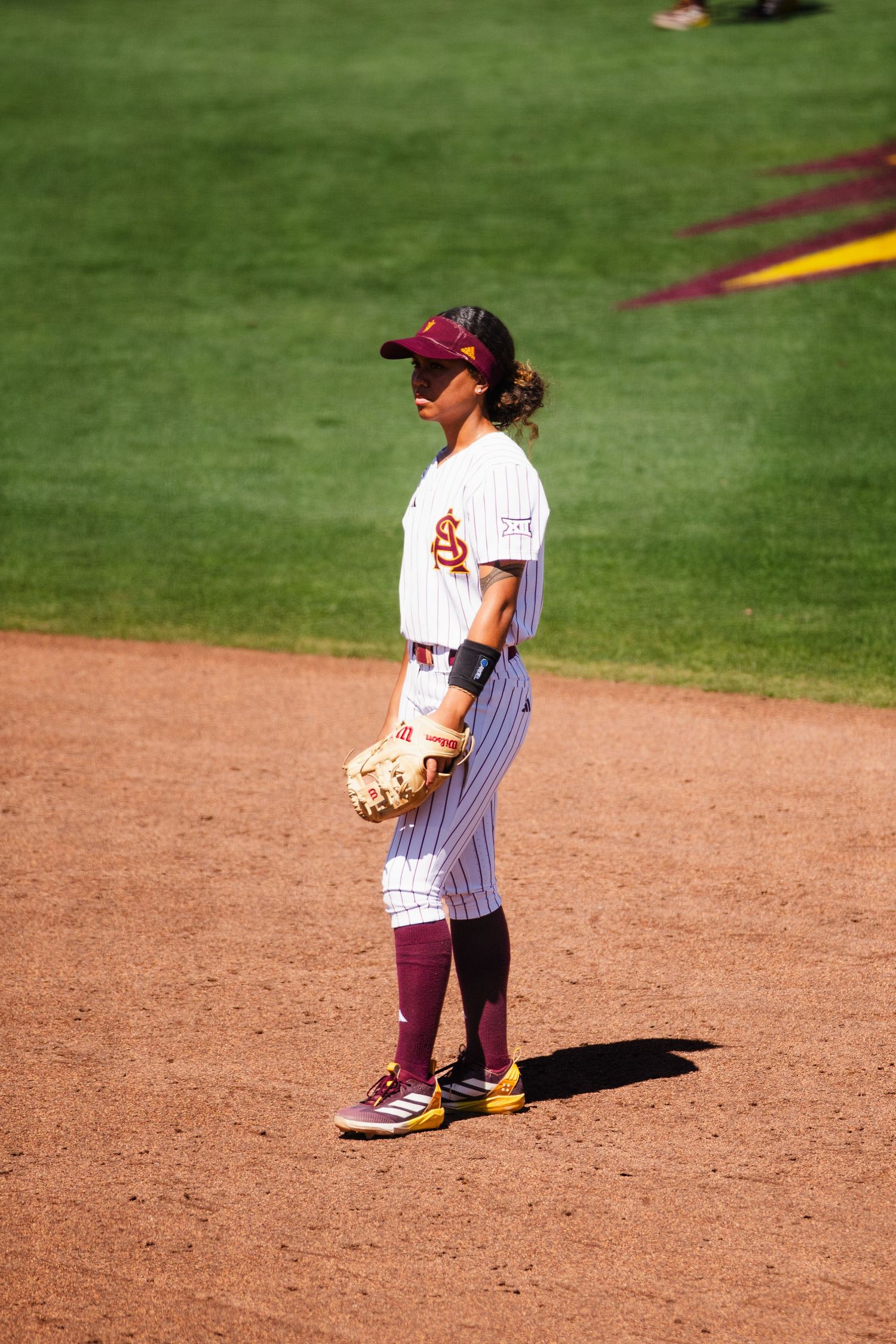 ASU Sun Devils softball player standing on field holding glove in pinstripe uniform.