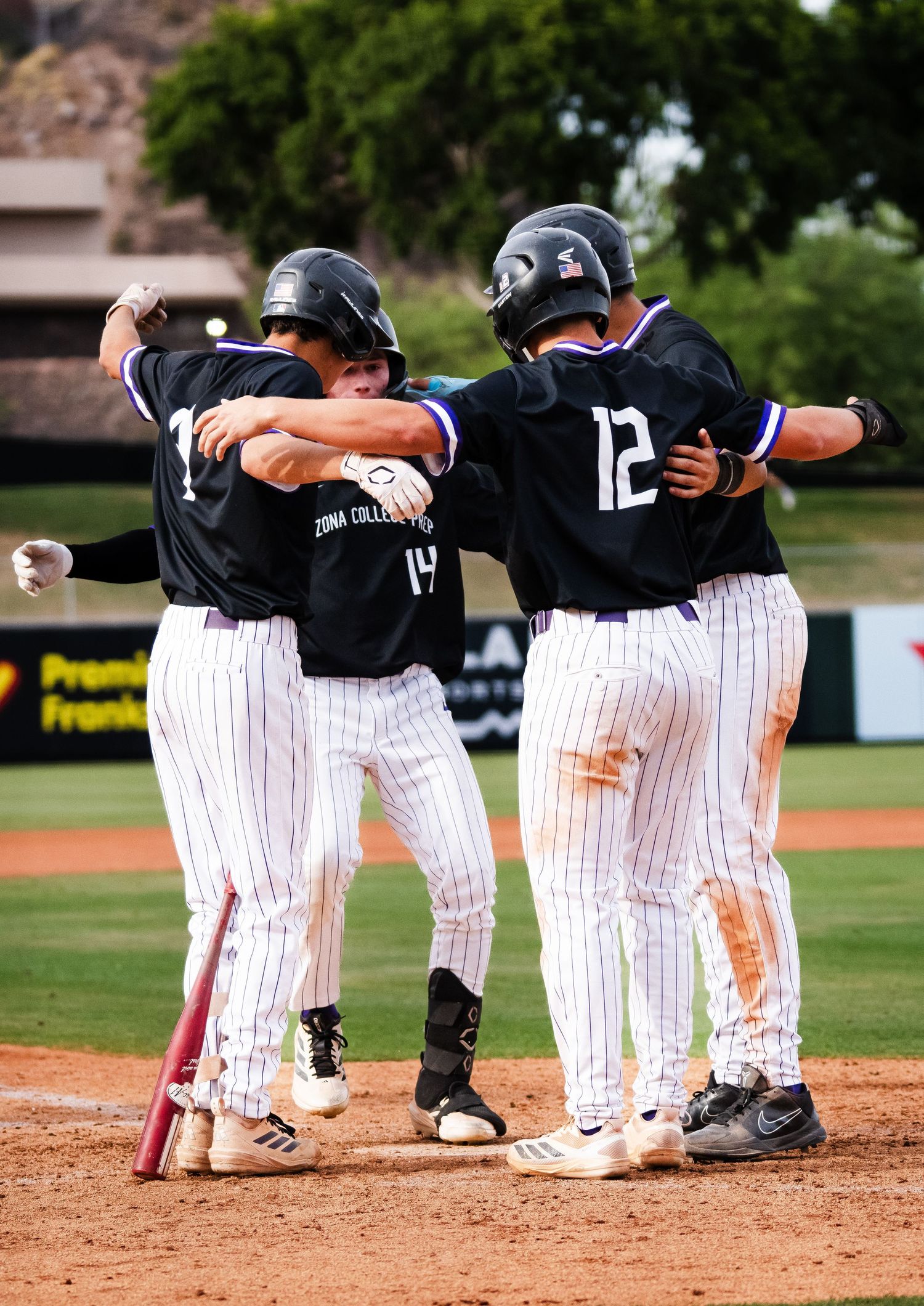 College baseball teammates in black pinstripe uniforms celebrating together on the field after a play.