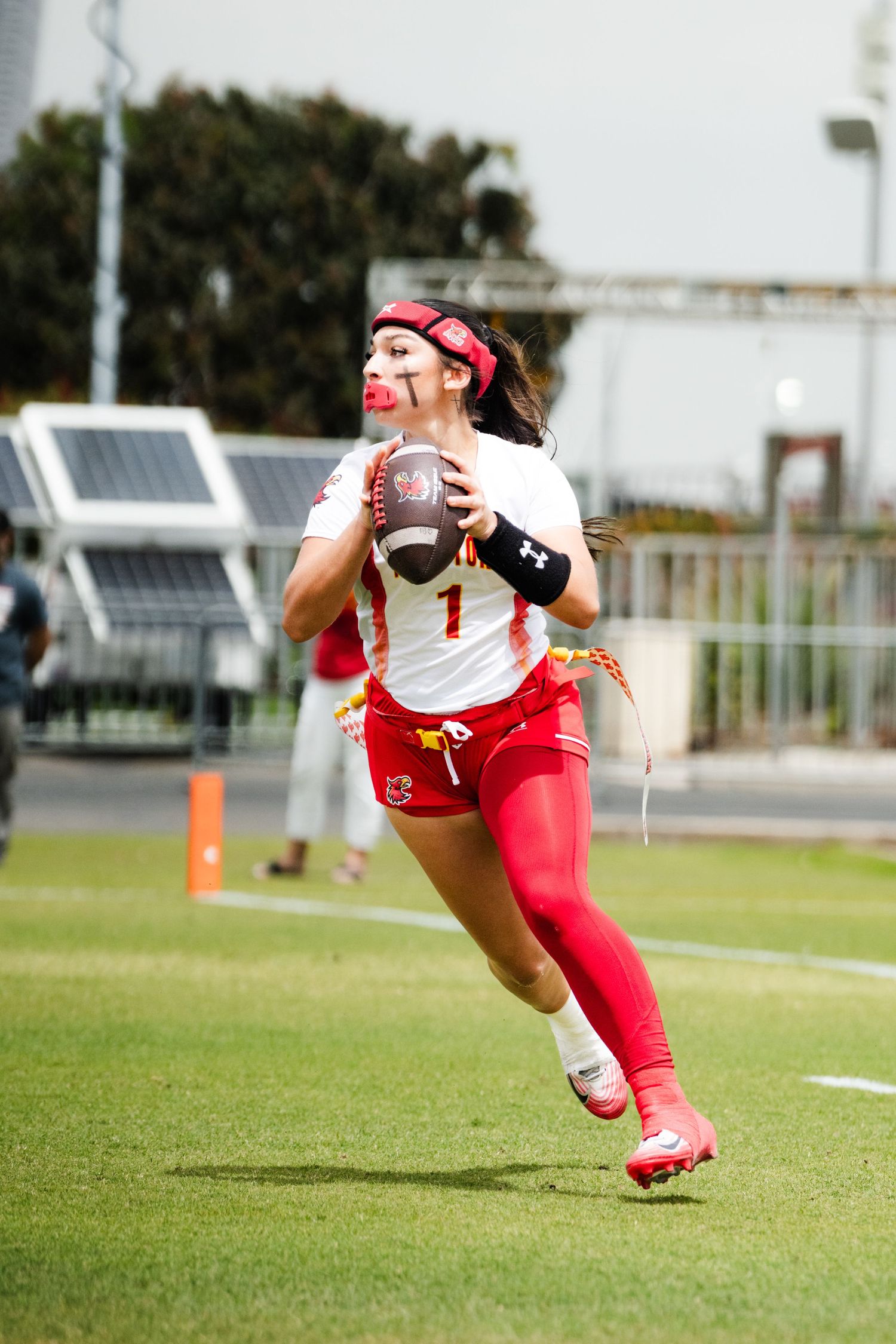 Female flag football player in red uniform catches a football while running on the field during a competitive game.