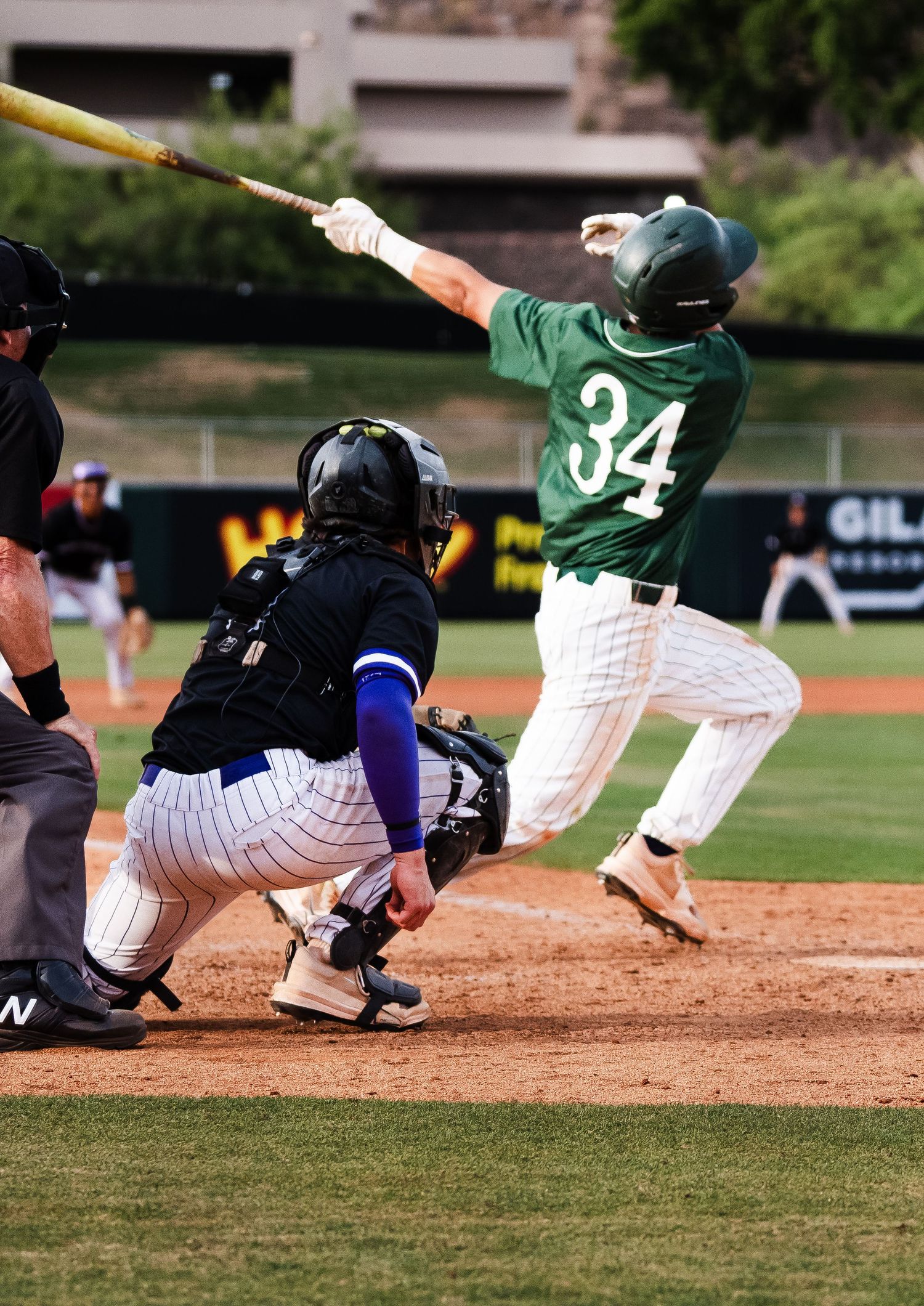 Baseball batter #34 in green uniform swings at pitch as catcher crouches behind home plate during game.