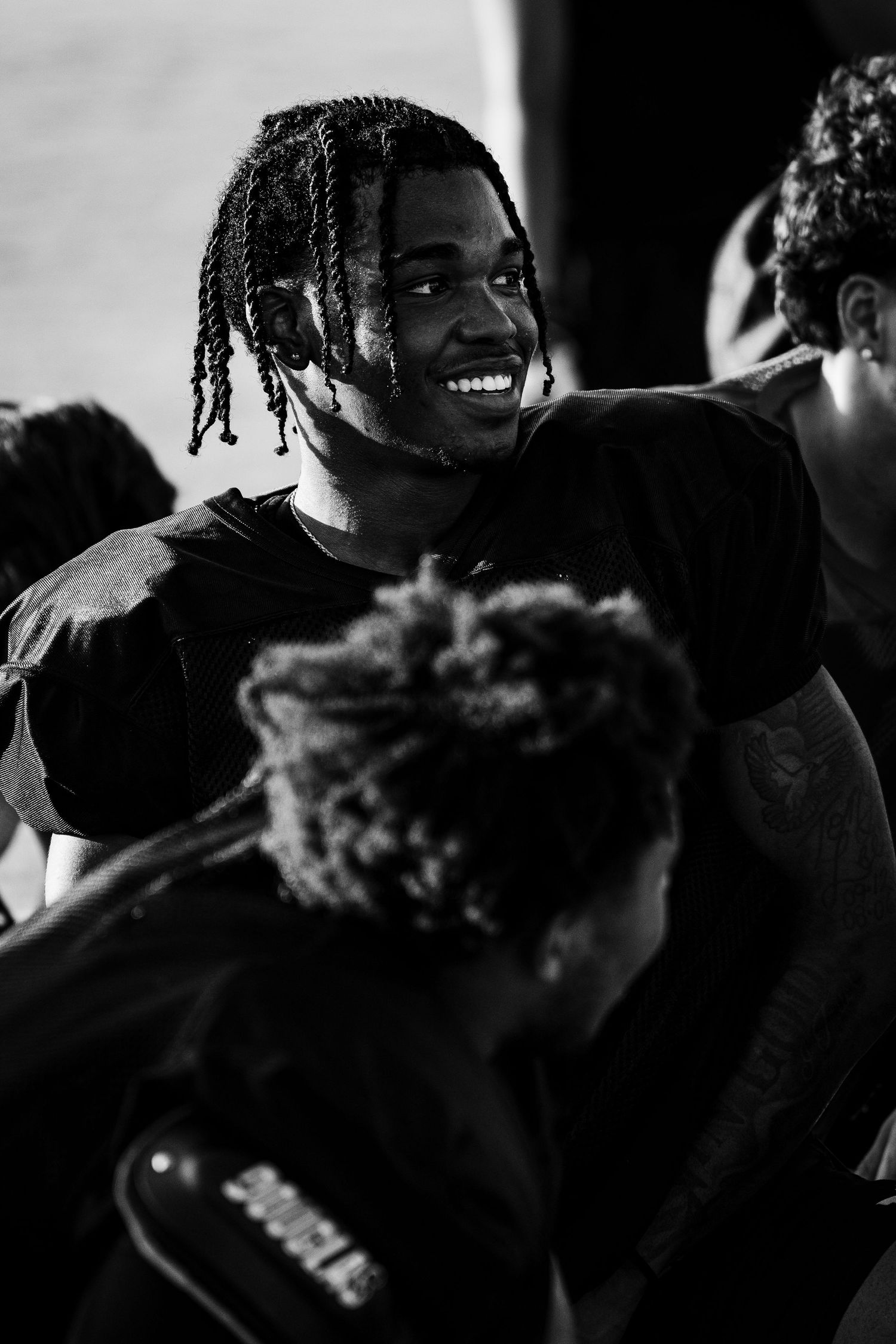 Black and white photo of a smiling young man with dreadlocks in a barbershop setting.