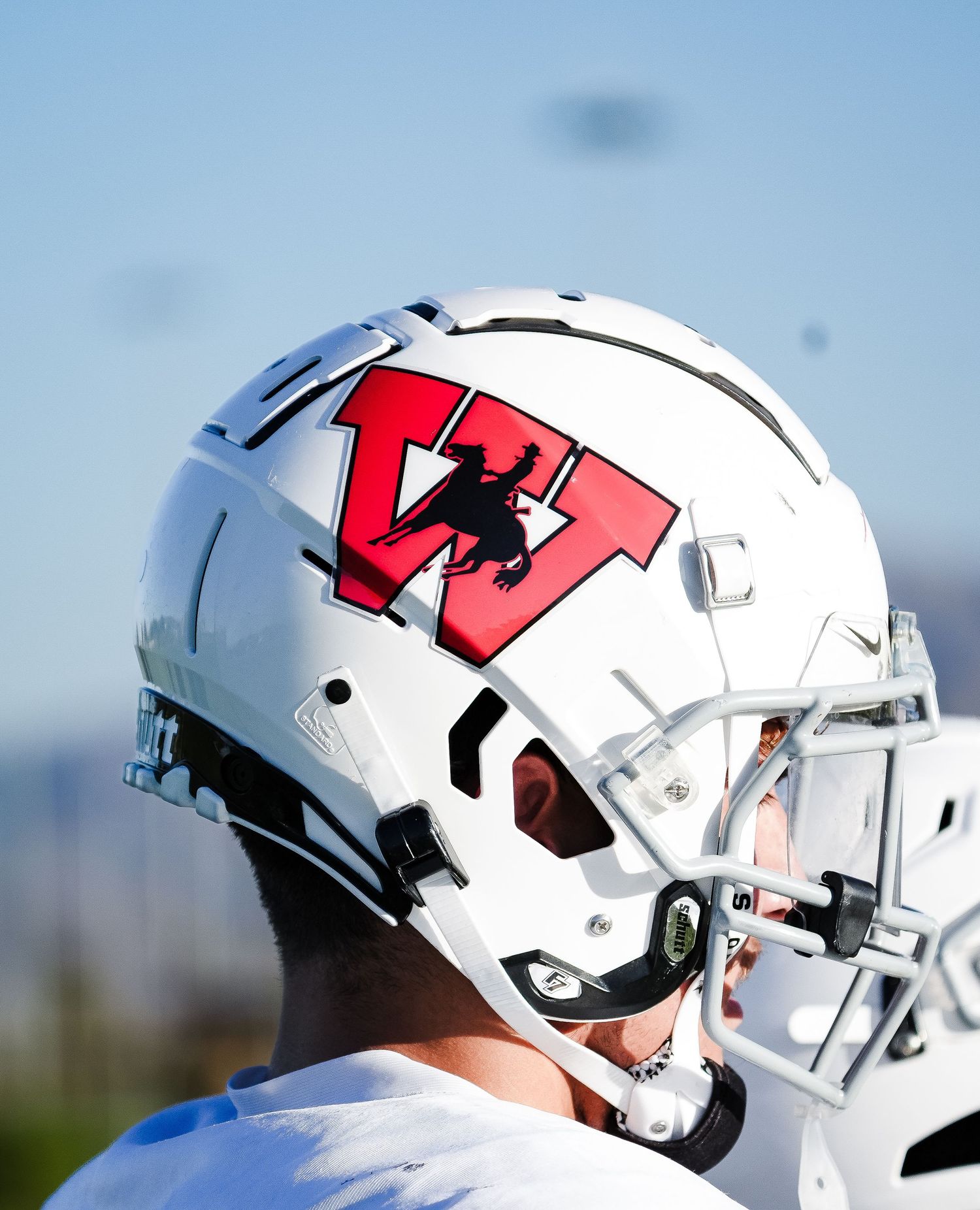 White football helmet with red W logo and black mascot silhouette, worn by a player on a sunny day.