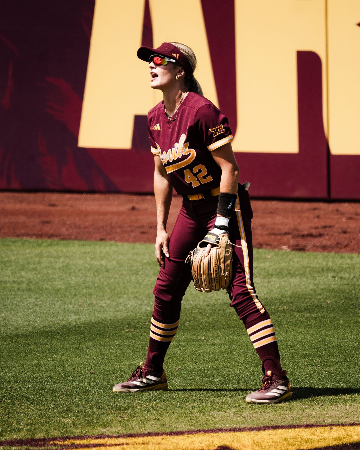 ASU softball player #42 in maroon uniform holds glove on sunny field.