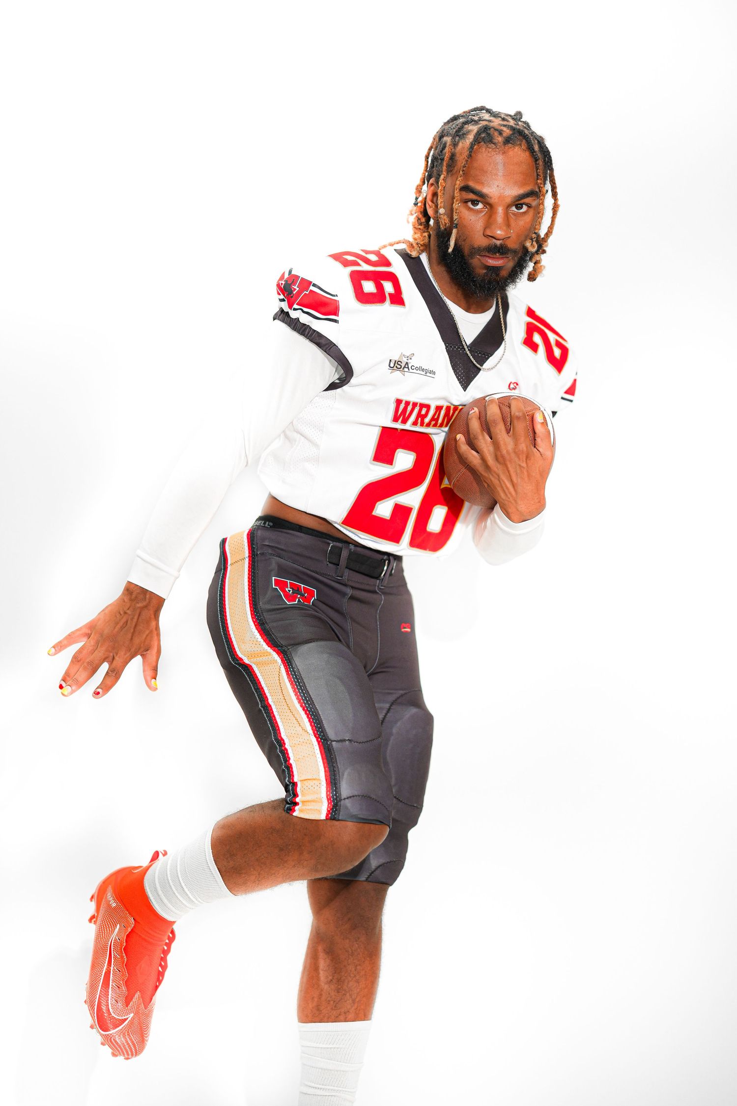 Football player in white Wranglers jersey number 26 poses dynamically holding a football, wearing red cleats on white background.