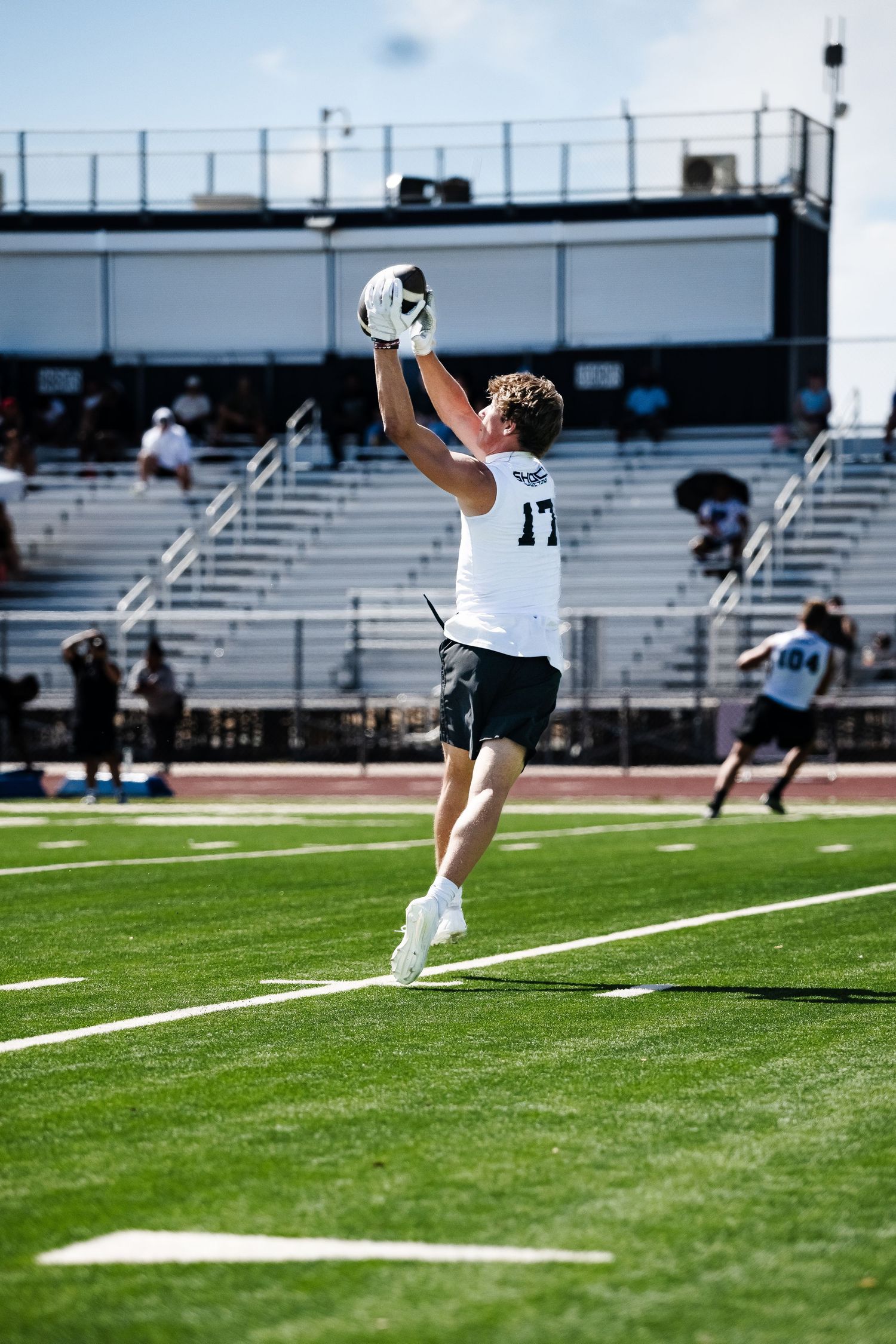 Football player number 17 leaps to make a catch during an outdoor training camp on a sunny day.