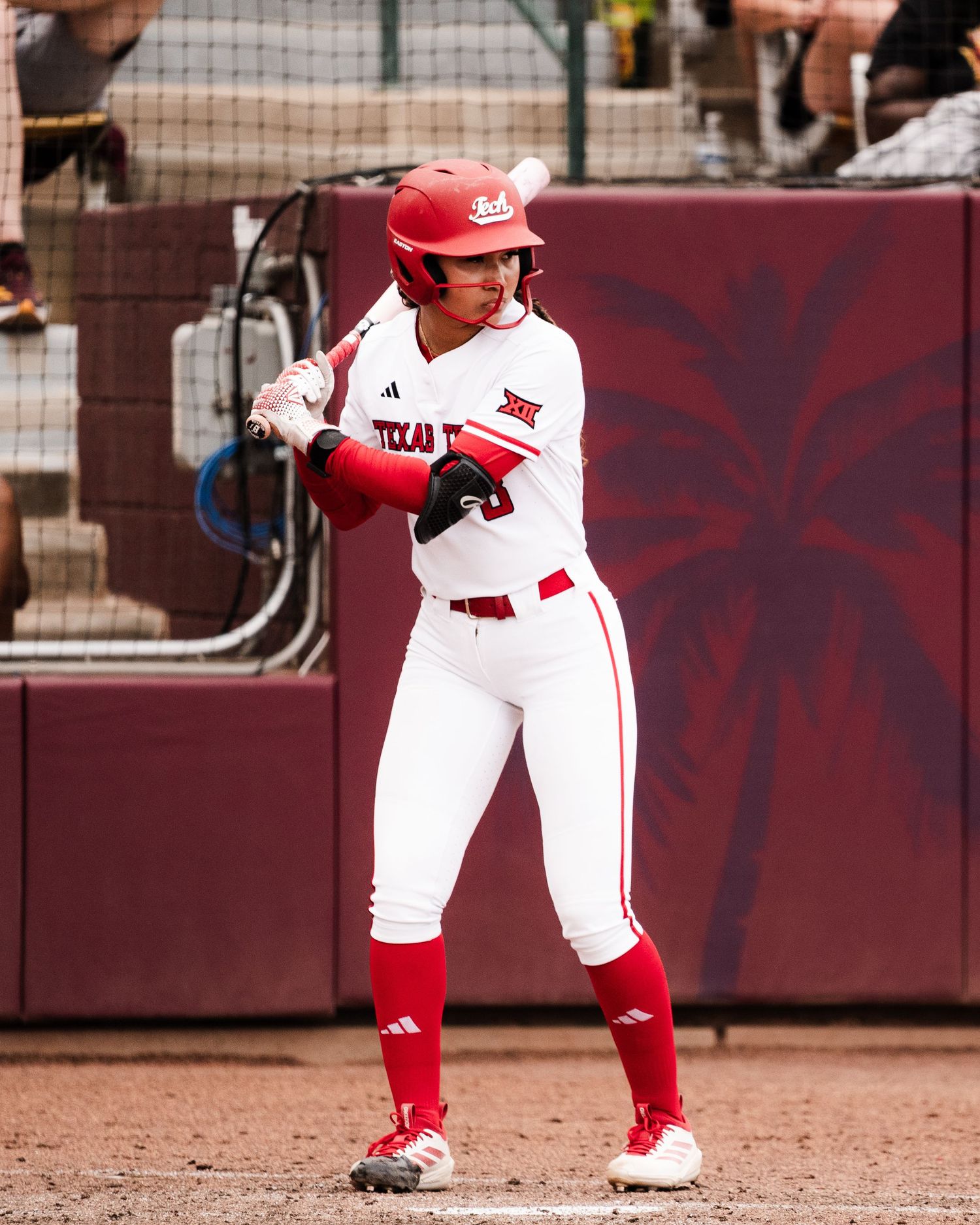 Texas Tech softball player in red and white uniform stands ready at bat during a college softball game.