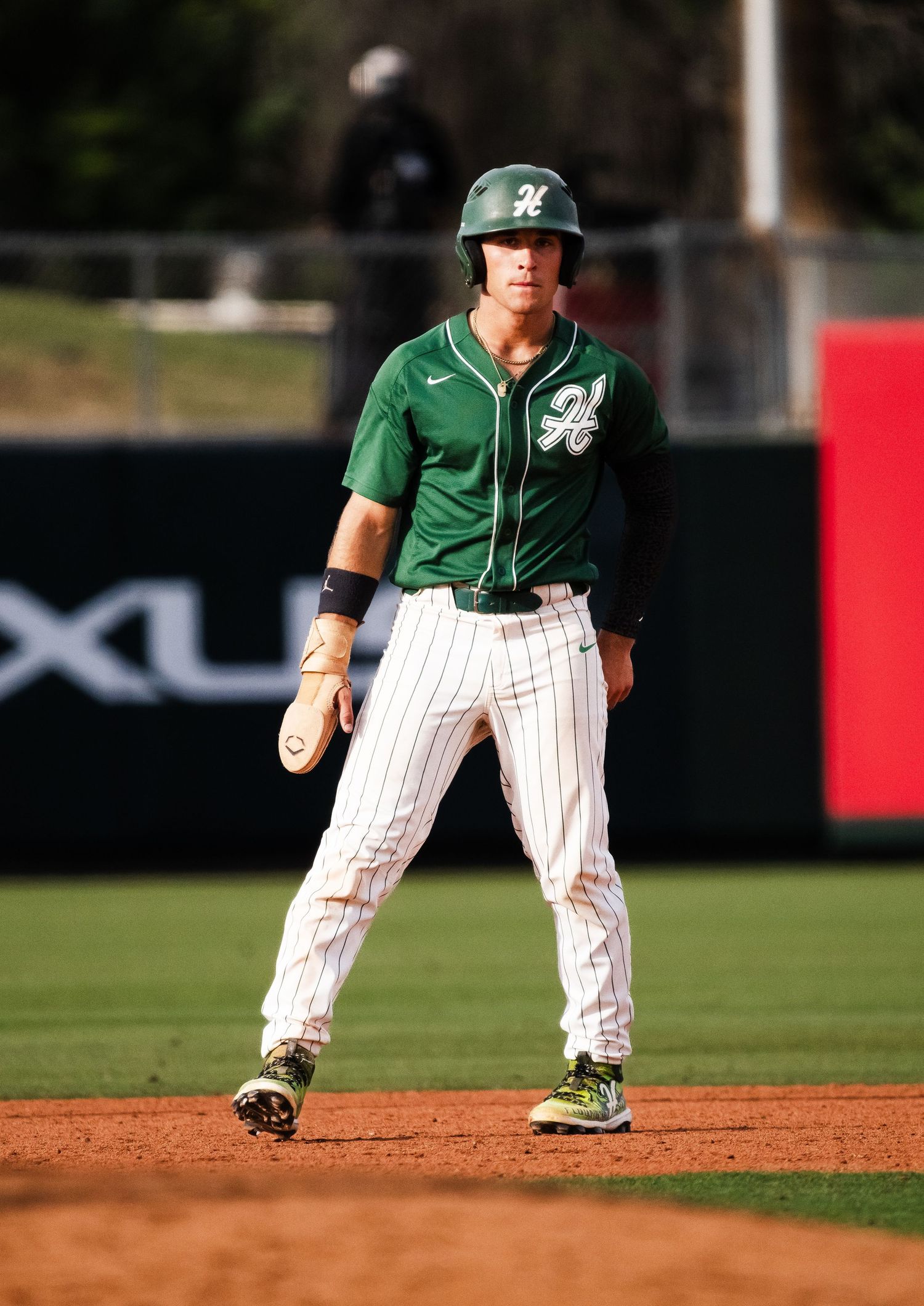 Baseball player in green Hawaii uniform stands ready on base during a game.