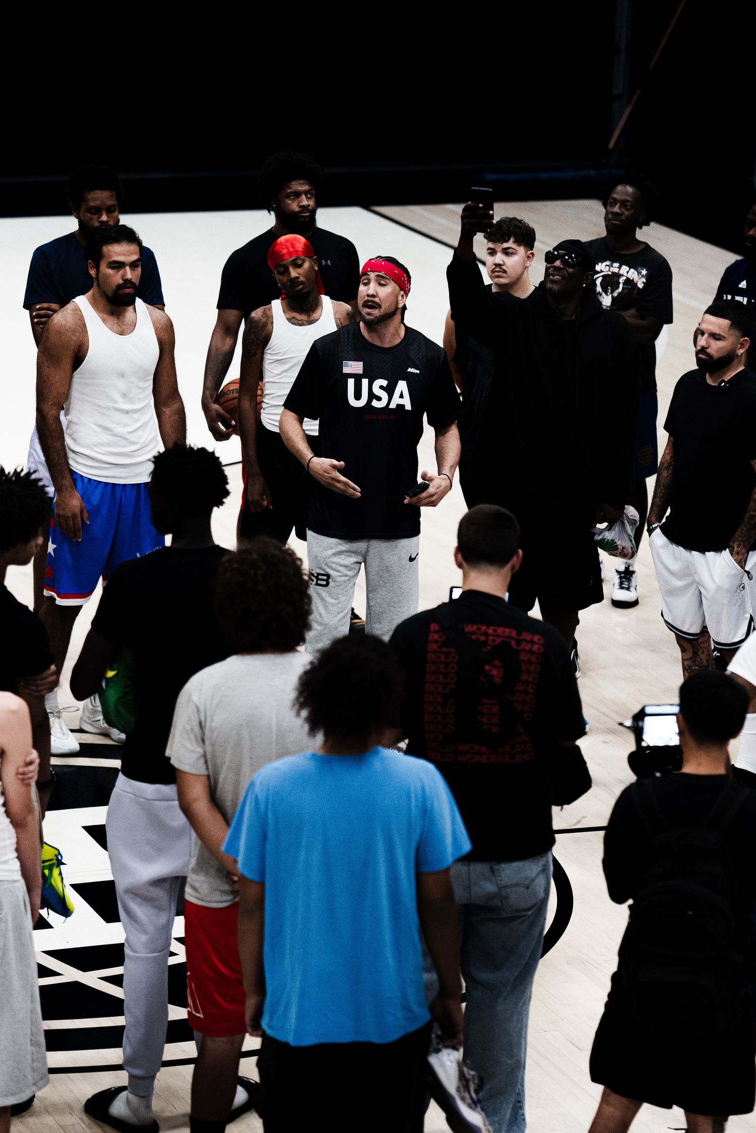 USA basketball team huddles on court during practice session with coach addressing players in arena.