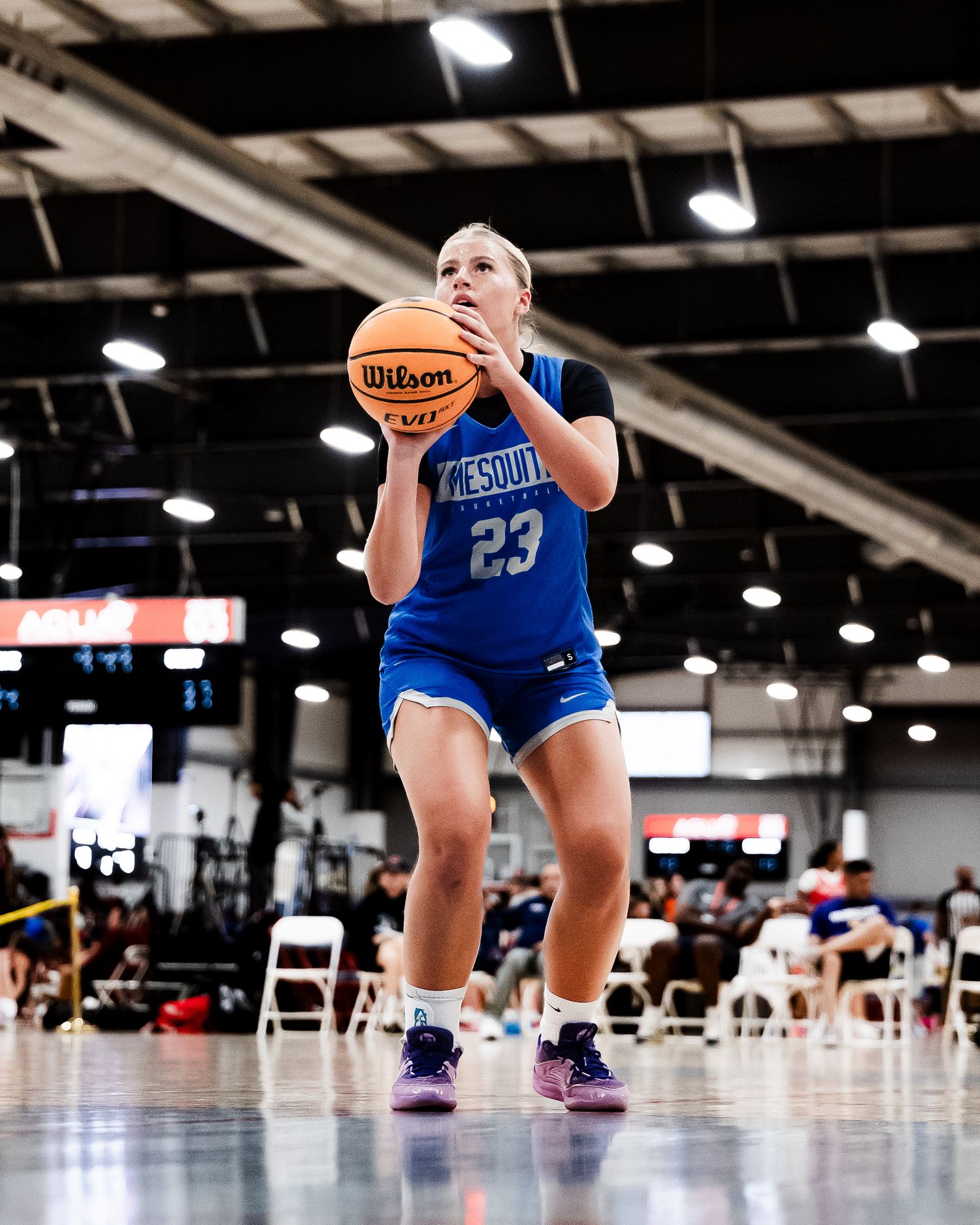 Female basketball player #23 in blue uniform prepares to shoot a Wilson basketball indoors.