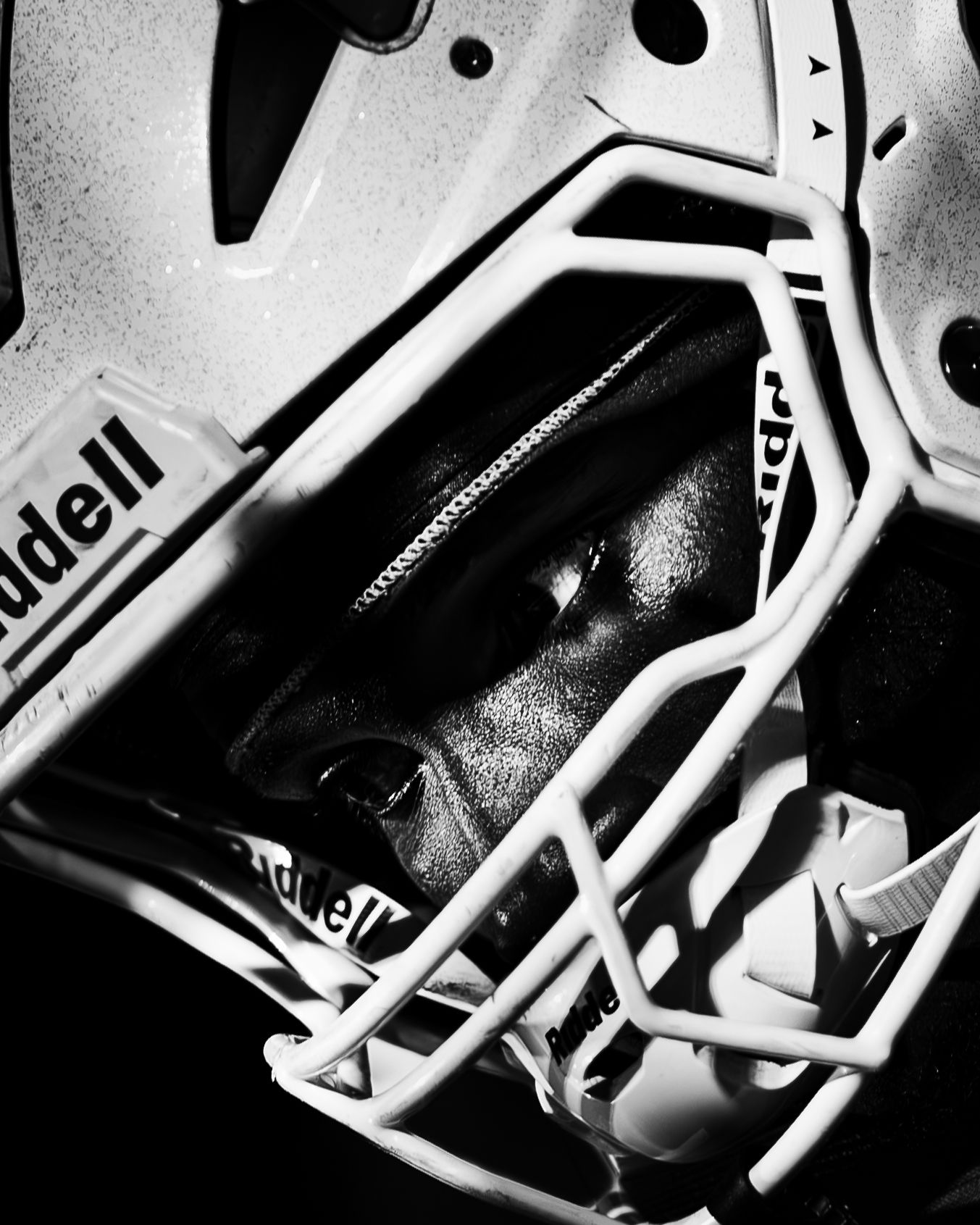 Close-up black and white photo of a Riddell football helmet with face mask, highlighting protective sports equipment detail.