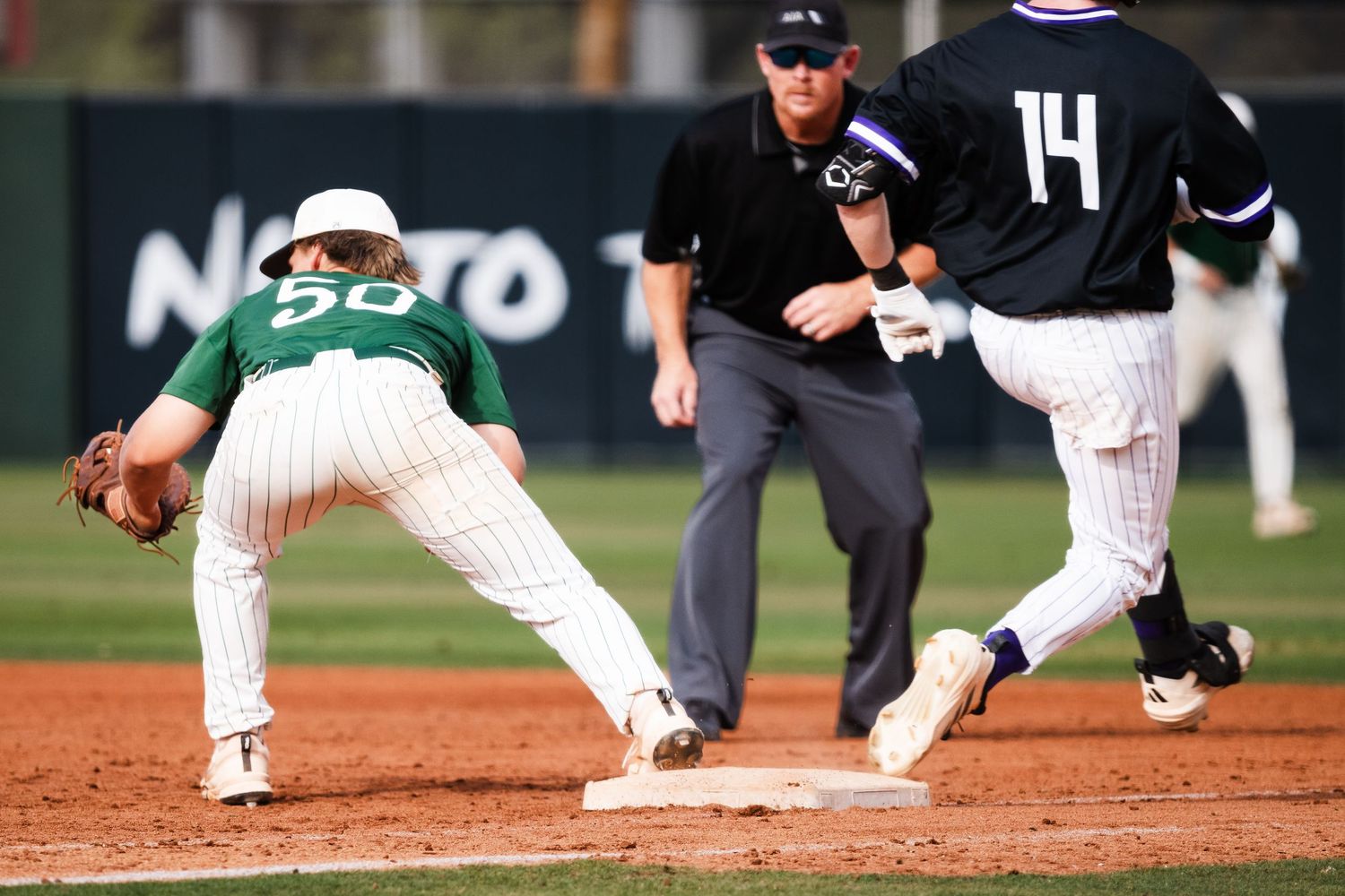 Baseball player #50 stretches to catch ball at first base as runner #14 approaches, with umpire watching closely.