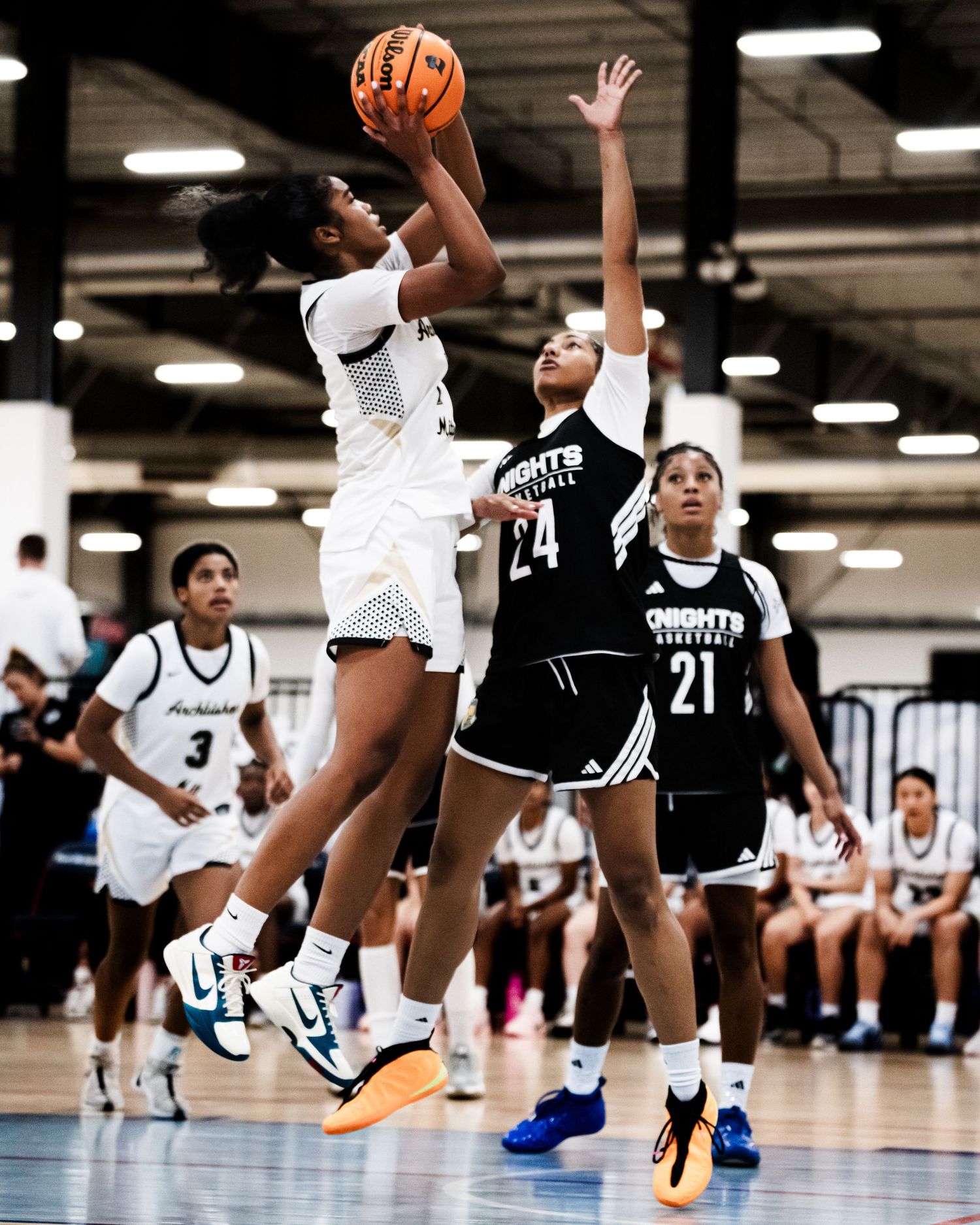 Female basketball player leaps for a layup against a defender in number 24 jersey during a competitive indoor game.