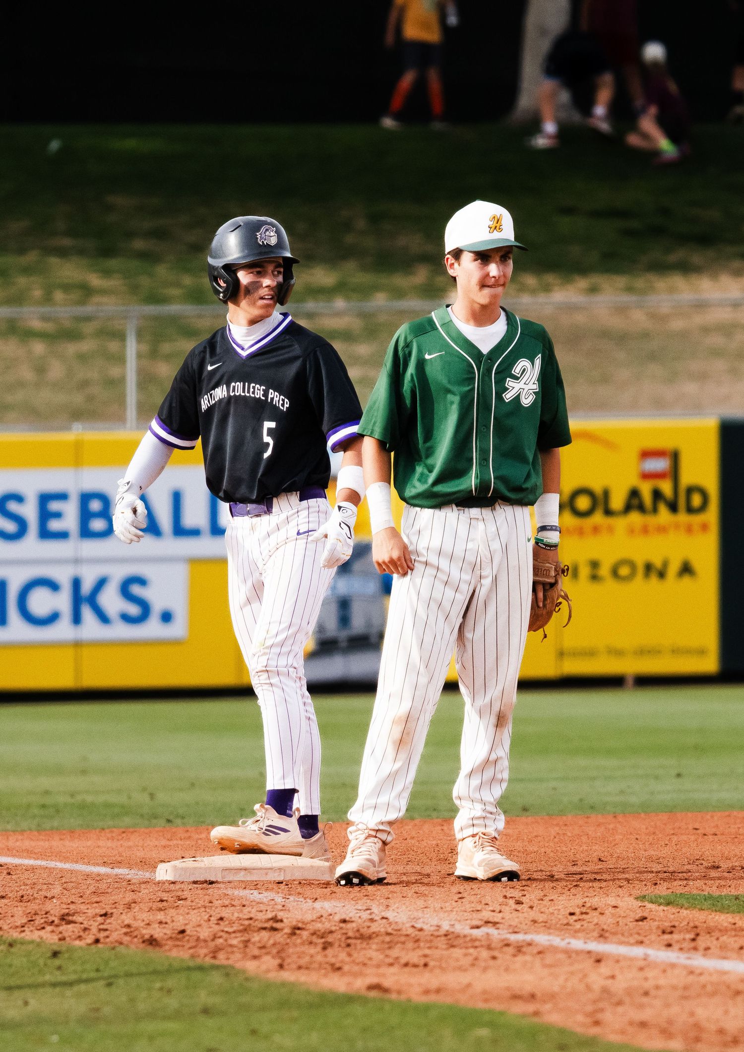 Arizona College Prep baseball player #5 stands on base next to a green-uniformed opposing fielder.