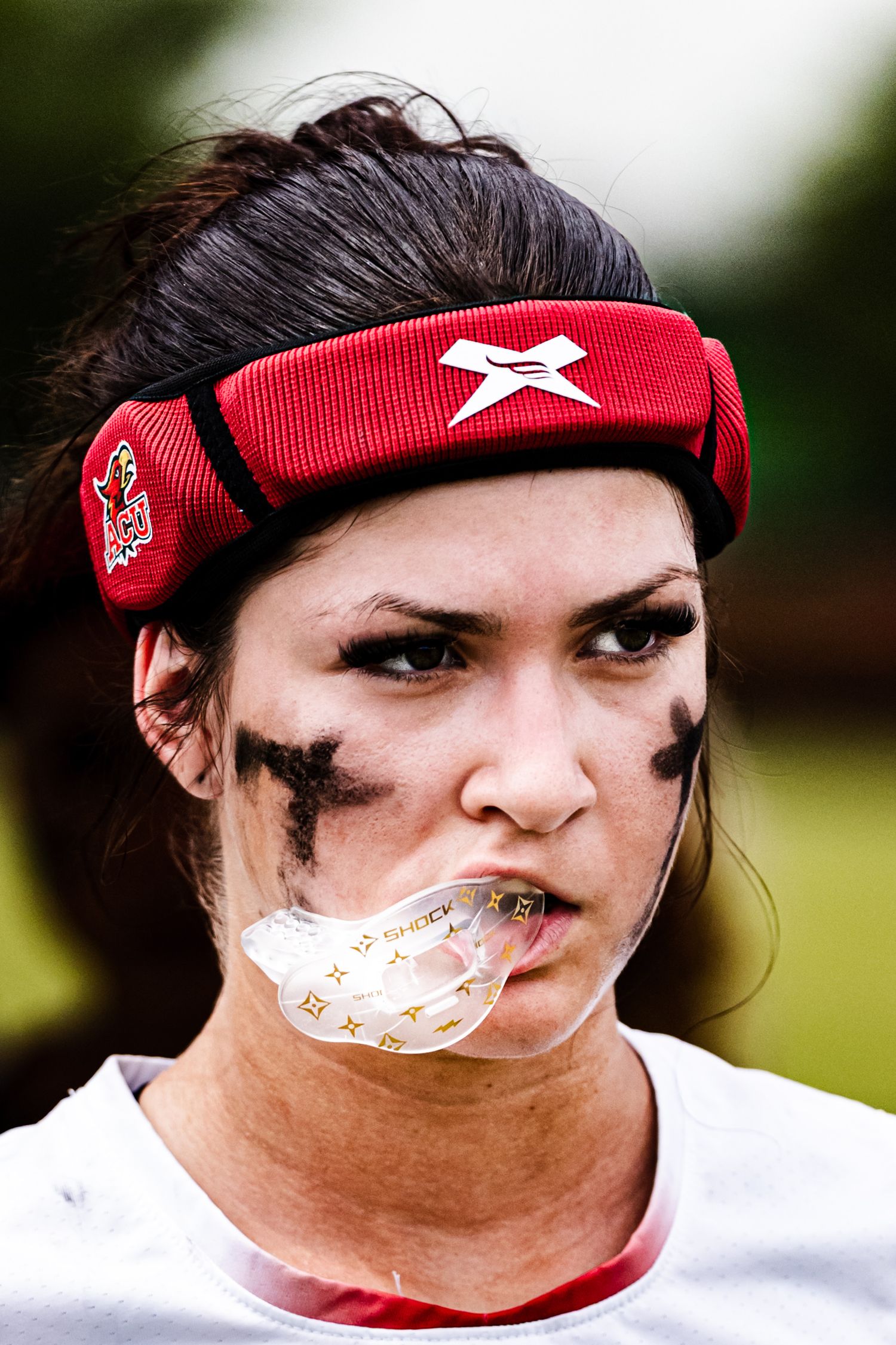 Female athlete with black face paint, red headband, and mouth guard ready for competition.
