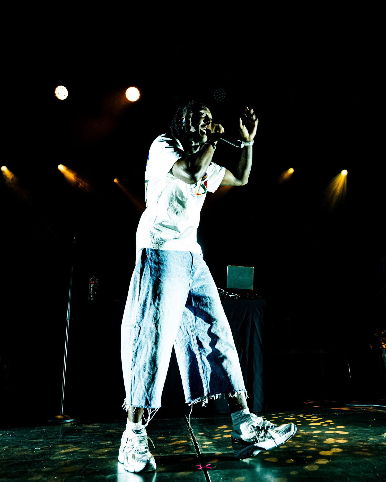 A singer in white outfit performs passionately on a dark stage with yellow concert lights.