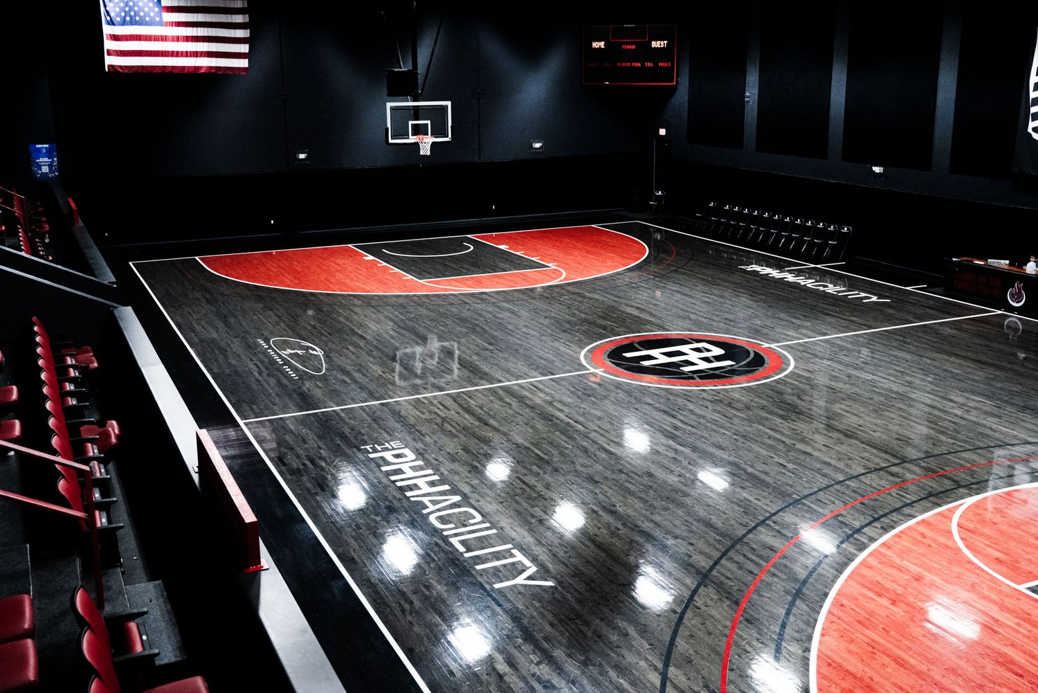 Modern indoor basketball court with bold red and black design, dramatic lighting, and American flag display.