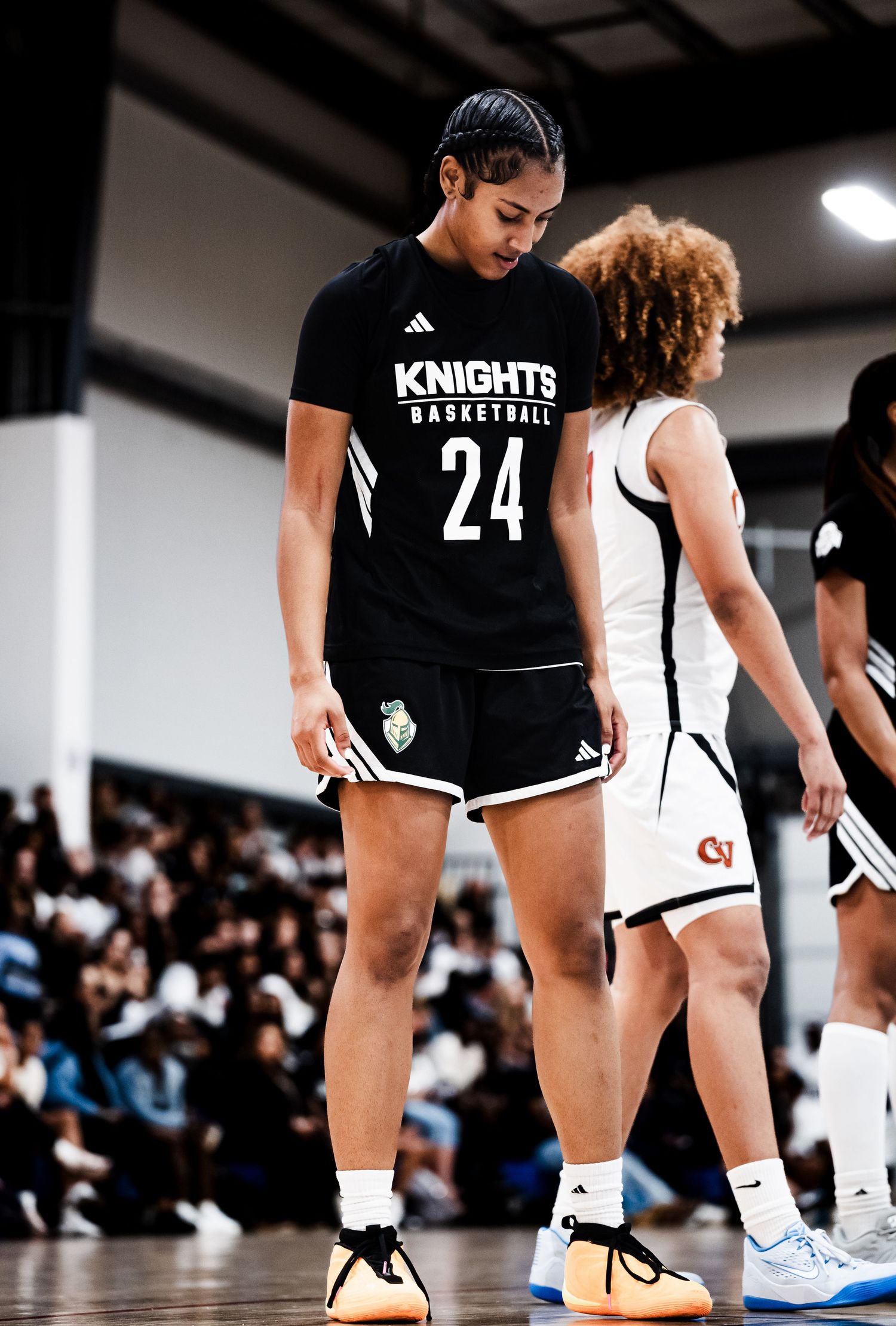 A tall Knights Basketball player wearing number 24 in black stands next to a shorter opponent during a girls basketball game.