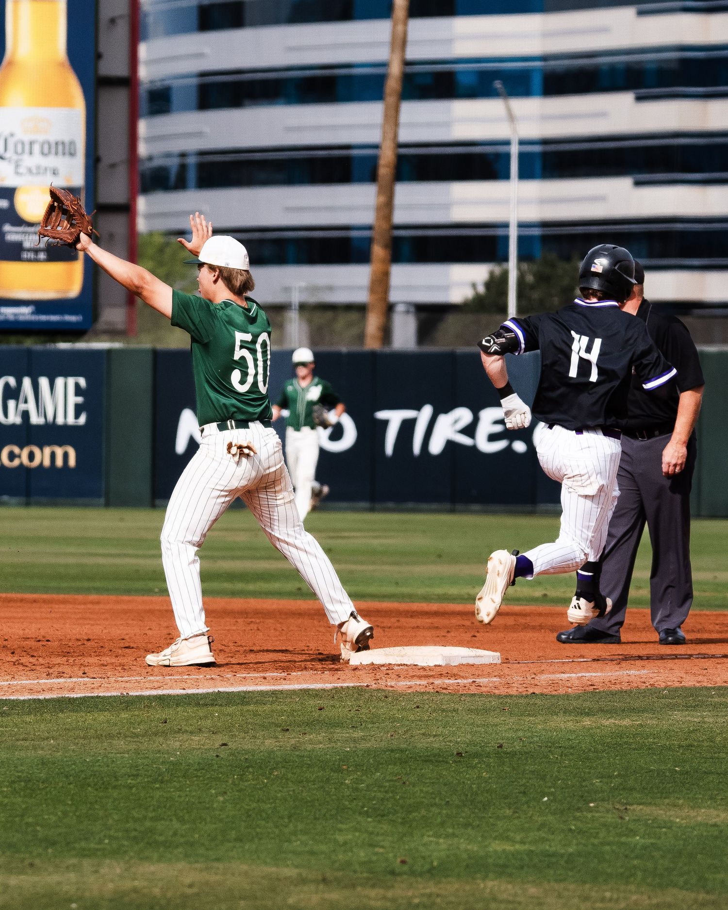 Baseball first baseman #50 stretches to catch ball as runner #14 approaches base during game.
