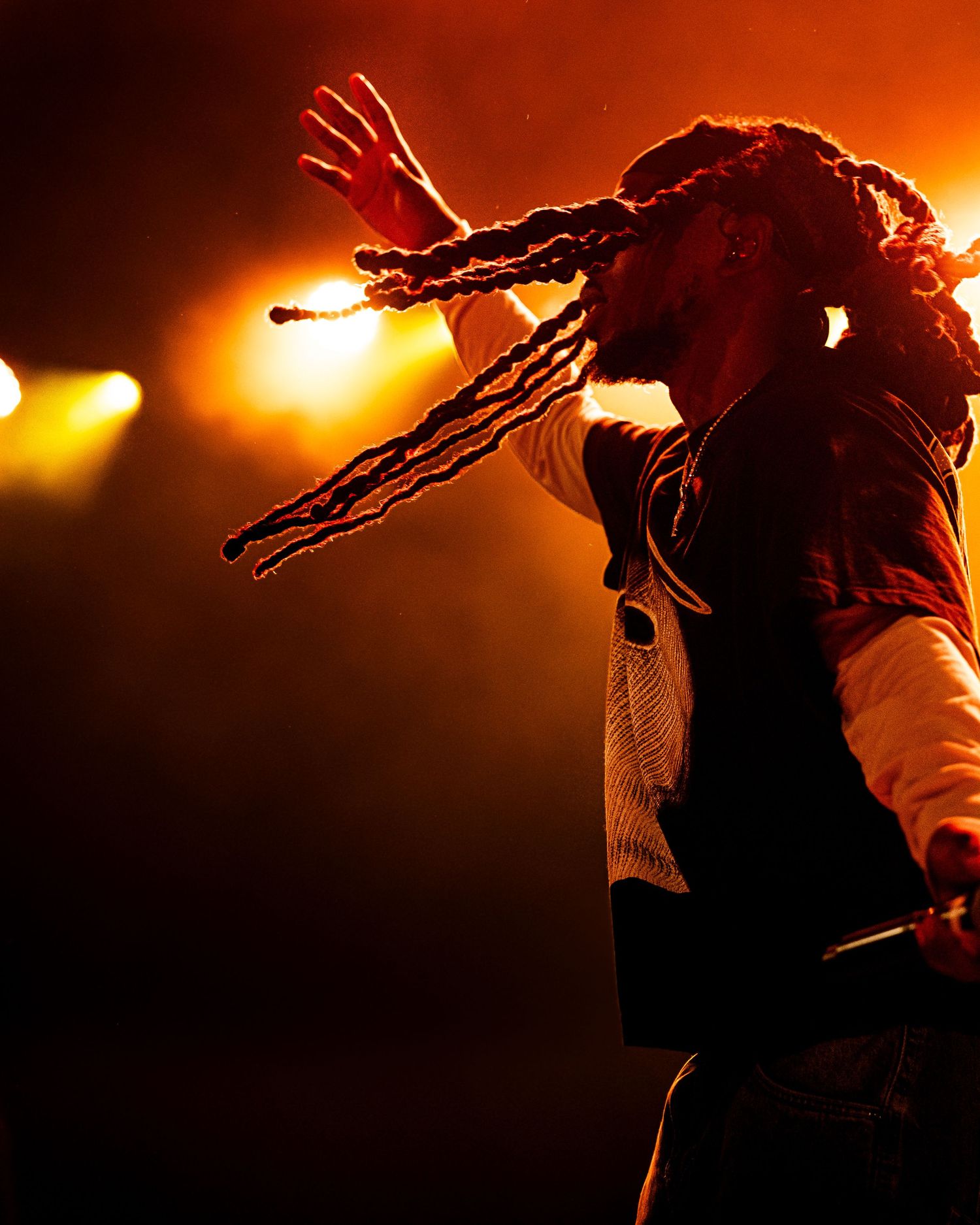 Reggae artist with dreadlocks performs passionately under warm orange stage lights at live music concert.