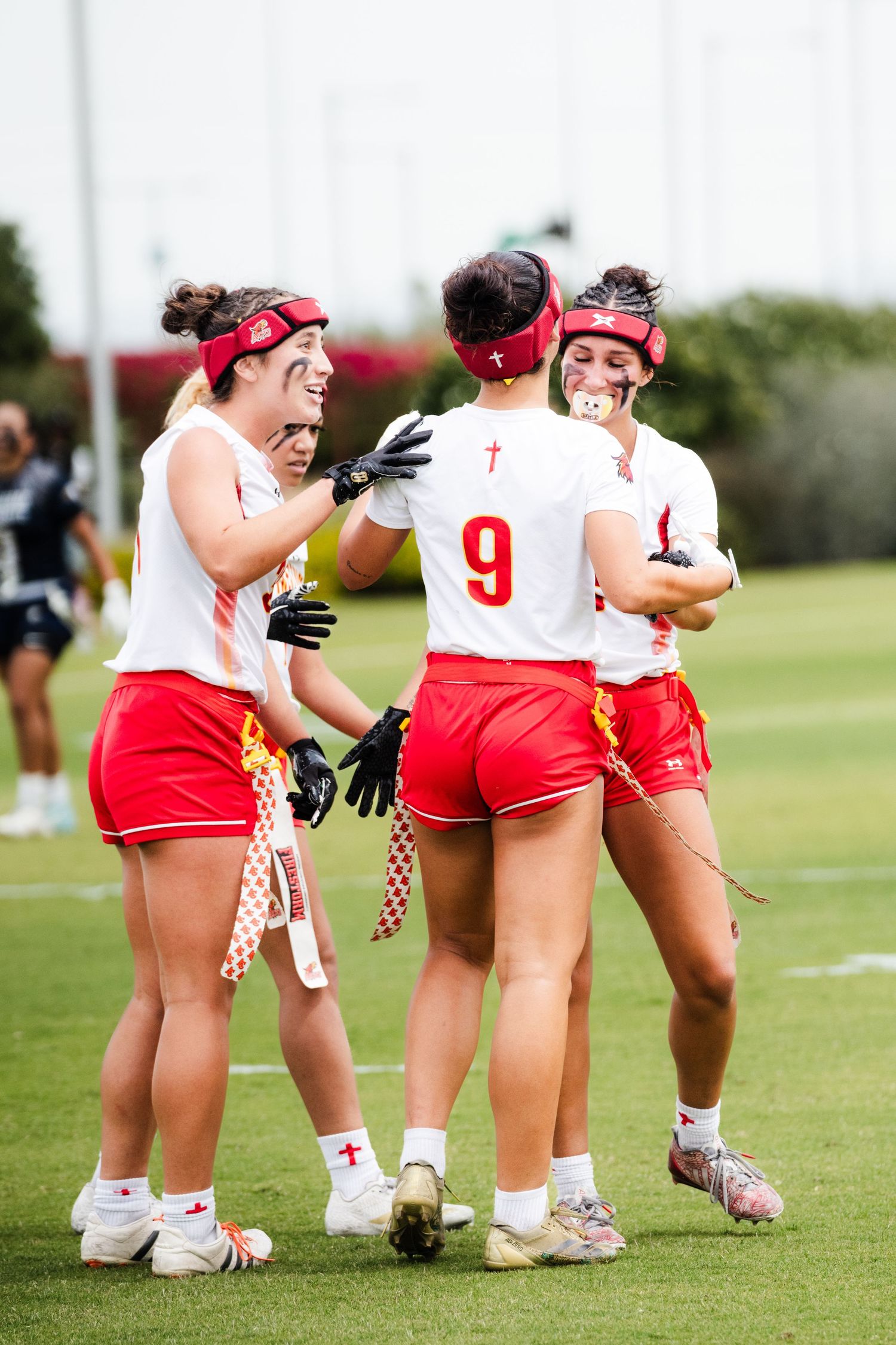 Female lacrosse players in red and white uniforms celebrate together on the field during a competitive game.
