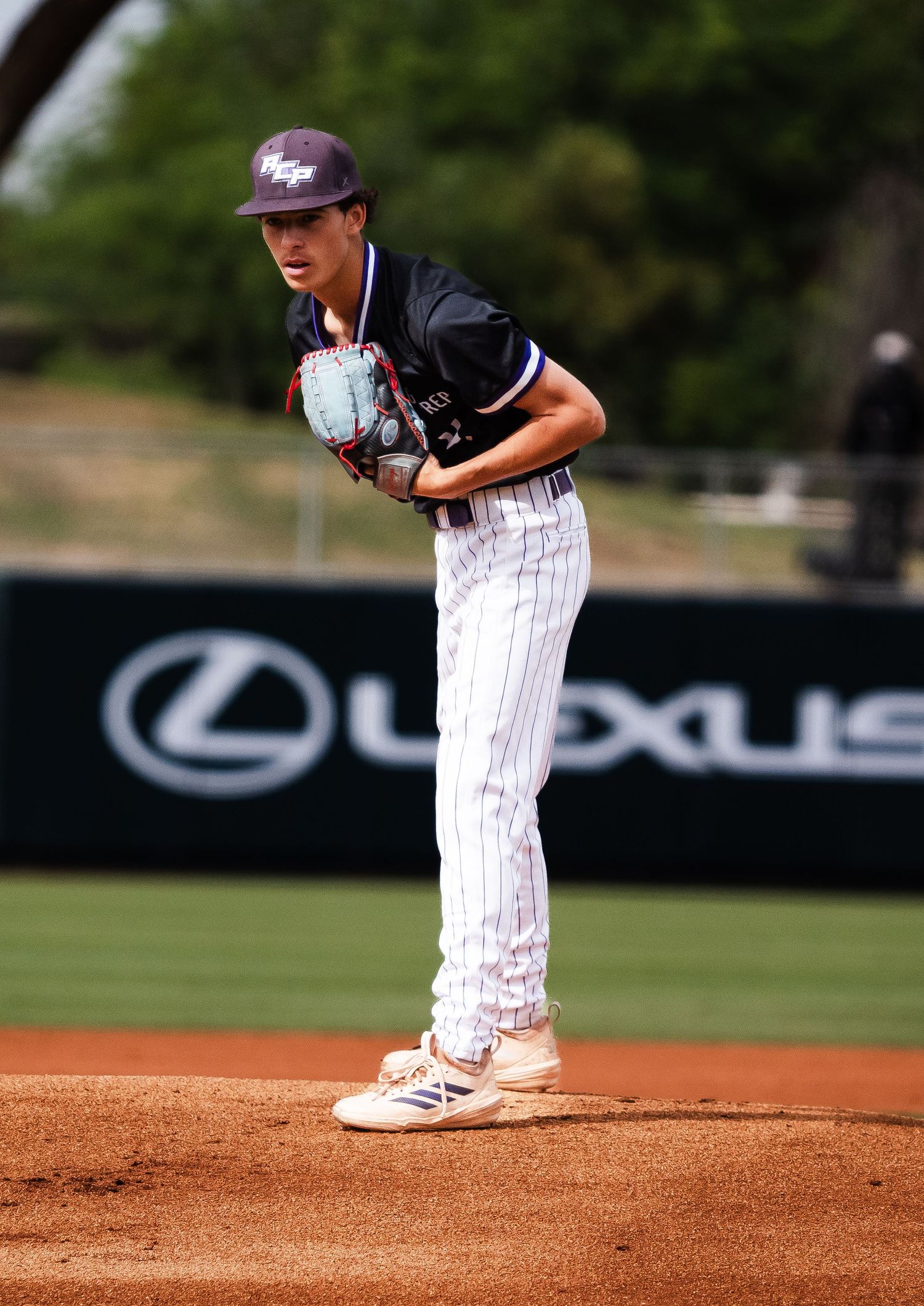 Arizona College Prep baseball pitcher in black pinstripe uniform winds up on the mound during a game.