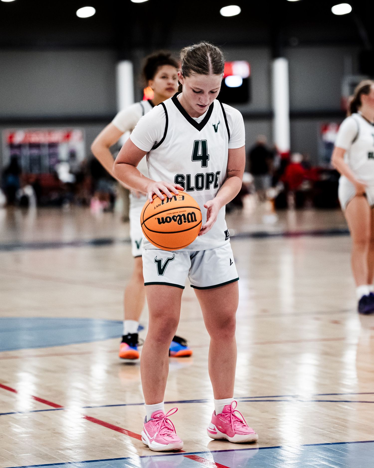 Female basketball player #4 in white Slope uniform holds Wilson basketball on indoor court.