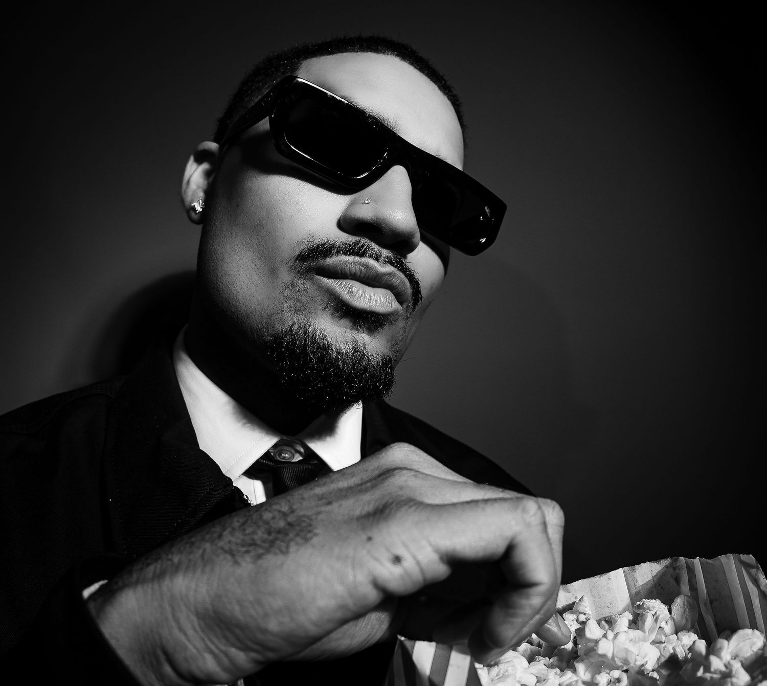 Man in sunglasses and suit holding popcorn, black and white portrait photo.