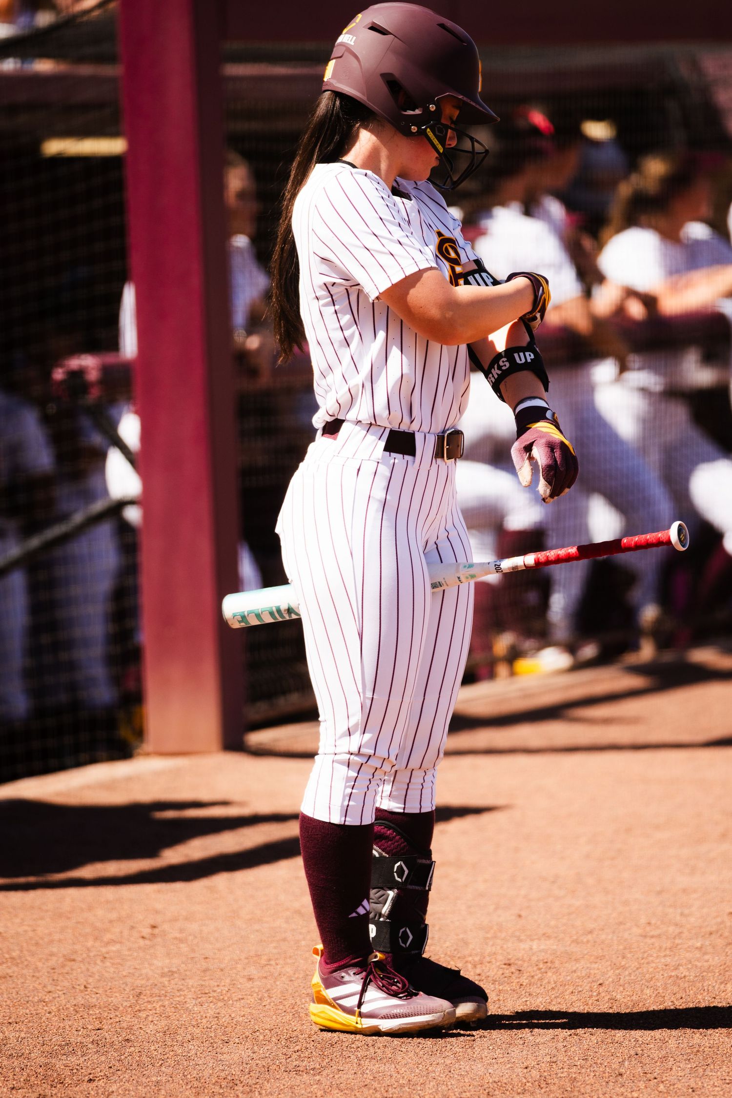 Female softball player in maroon pinstripe uniform and helmet prepares to bat during a college softball game.