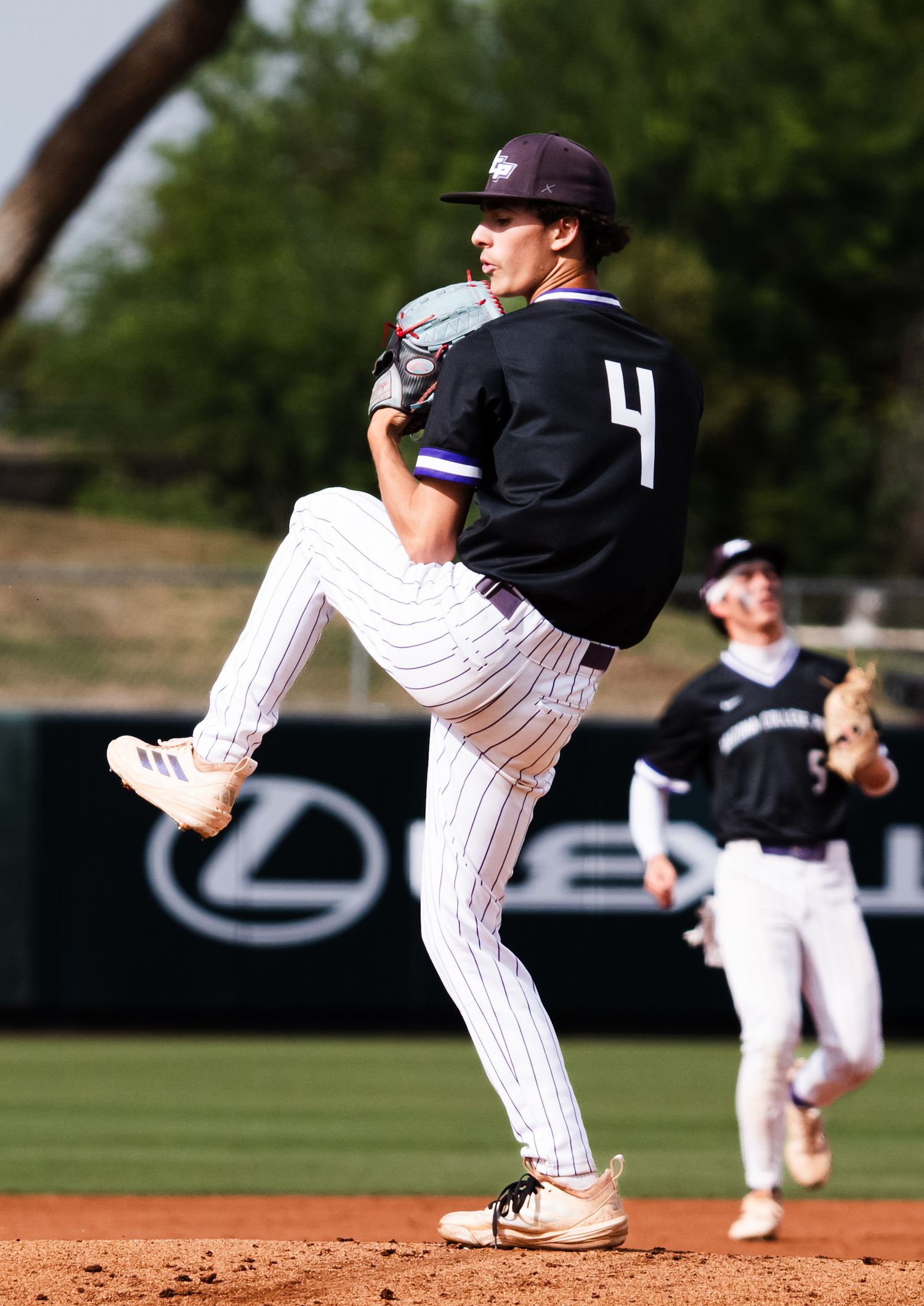Baseball pitcher number 4 in black uniform winds up to throw during a competitive game.