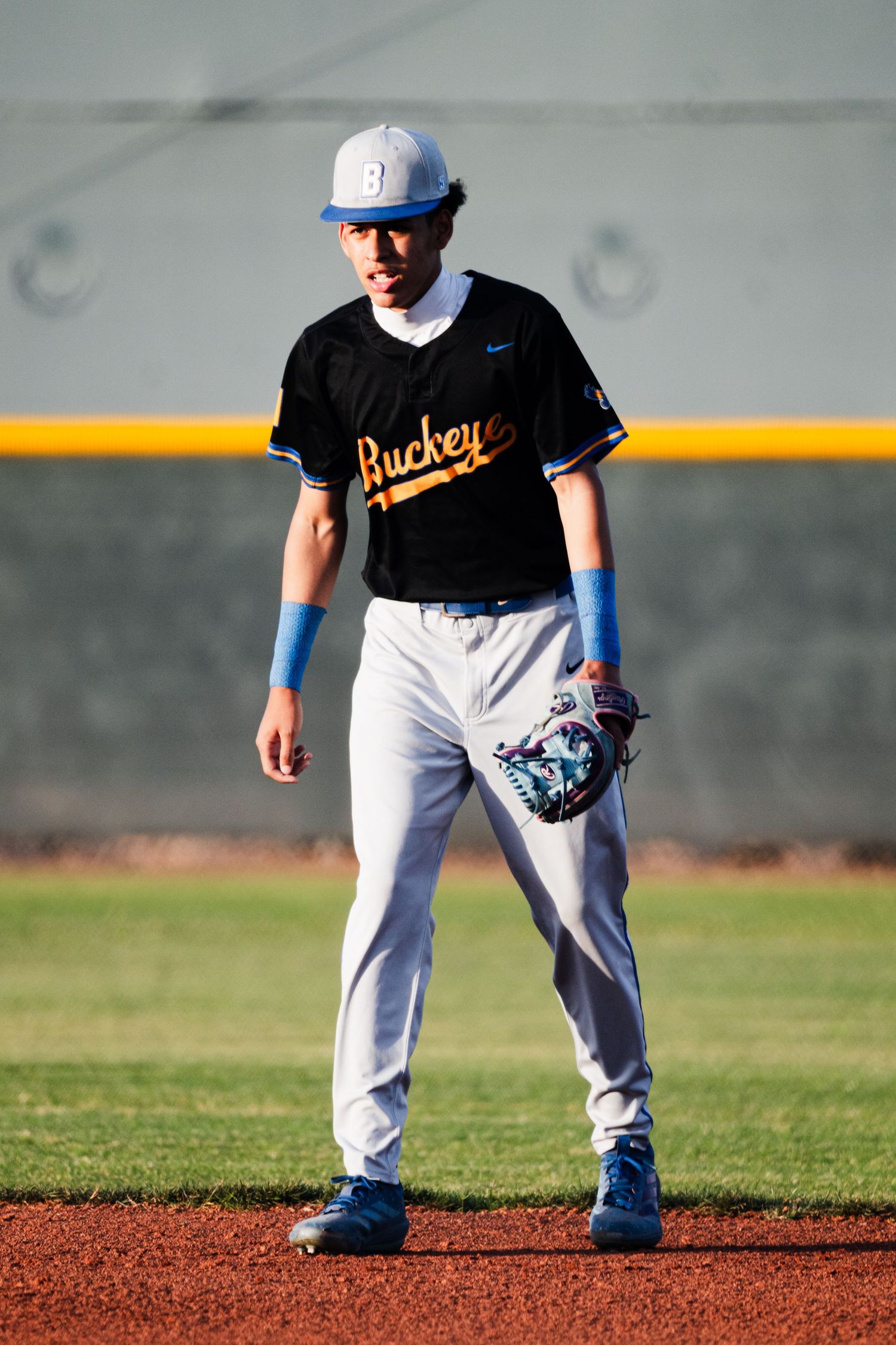 Baseball player in Buckeyes black jersey and gray pants stands ready on the field wearing a glove.