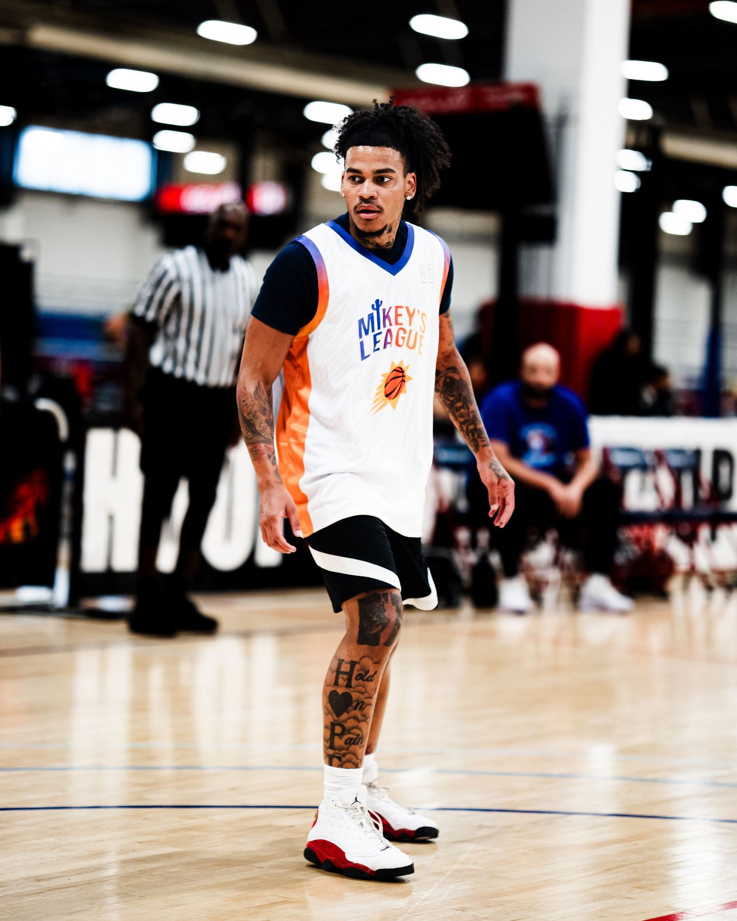 Tattooed basketball player in Mikey League jersey dribbles on indoor court during a game.