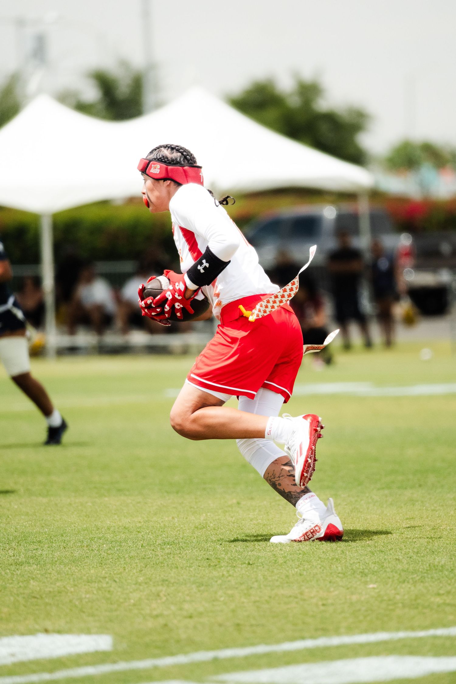 Football player in red and white uniform catching a ball during an outdoor flag football game on a green field.