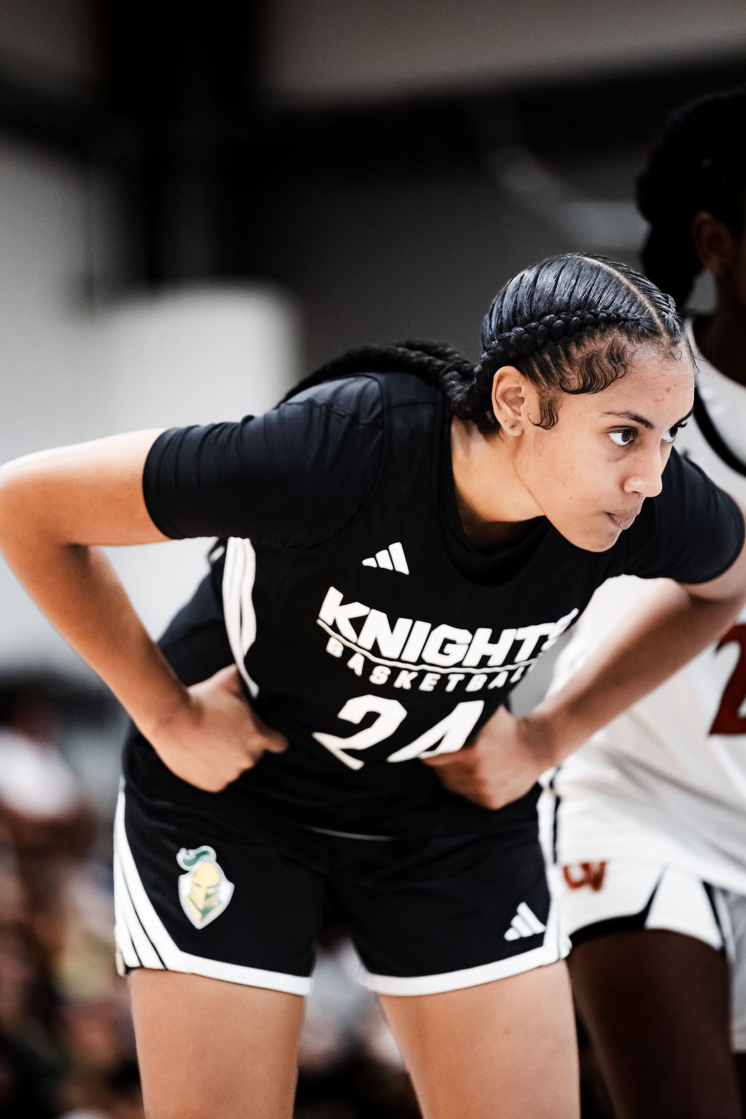 Female basketball player #24 in black Knights Basketball uniform stands with hands on hips during game.