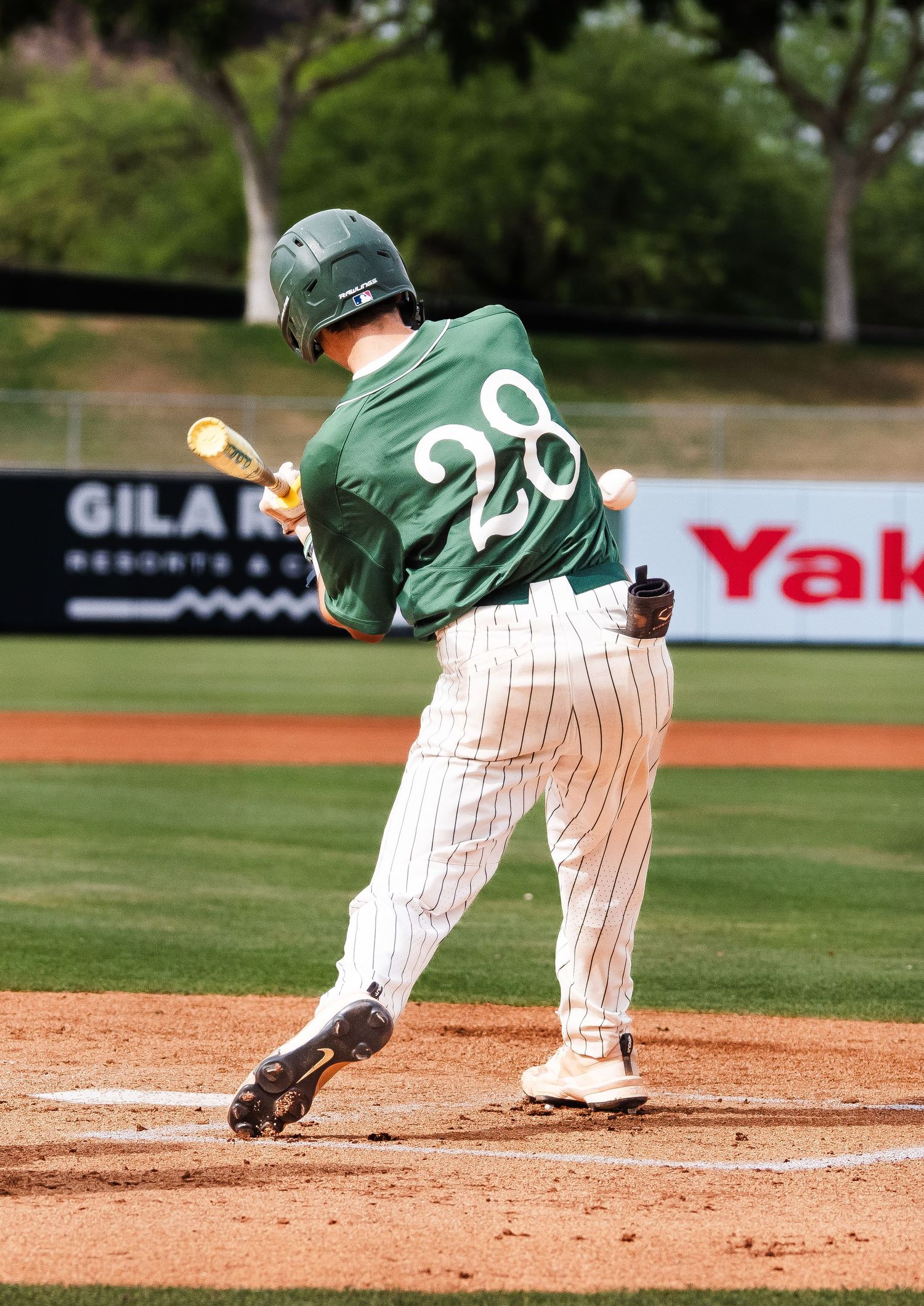 Baseball batter in green number 28 jersey making contact with pitch.