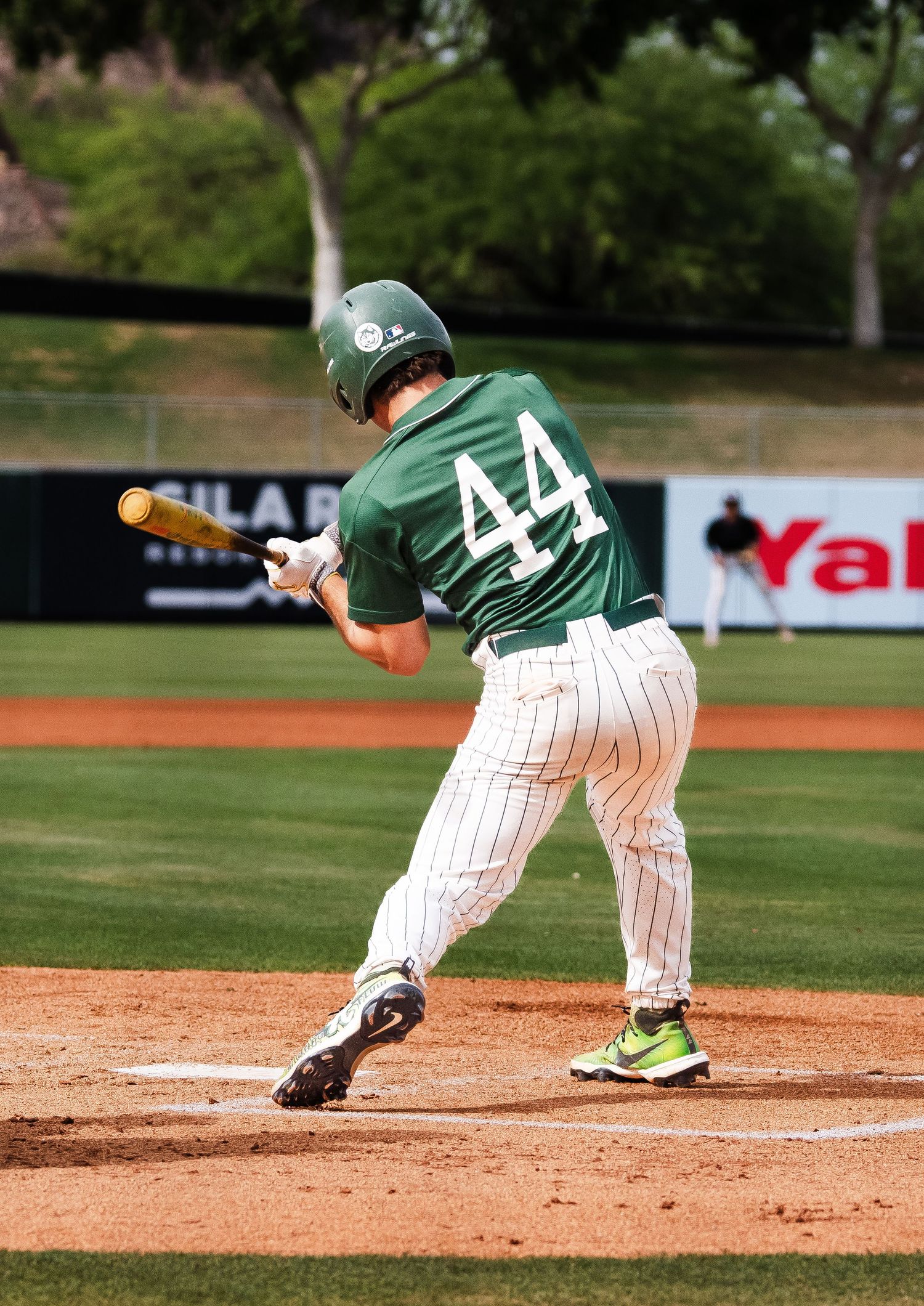 Baseball player number 44 in green uniform swinging bat during a game on a sunny day.