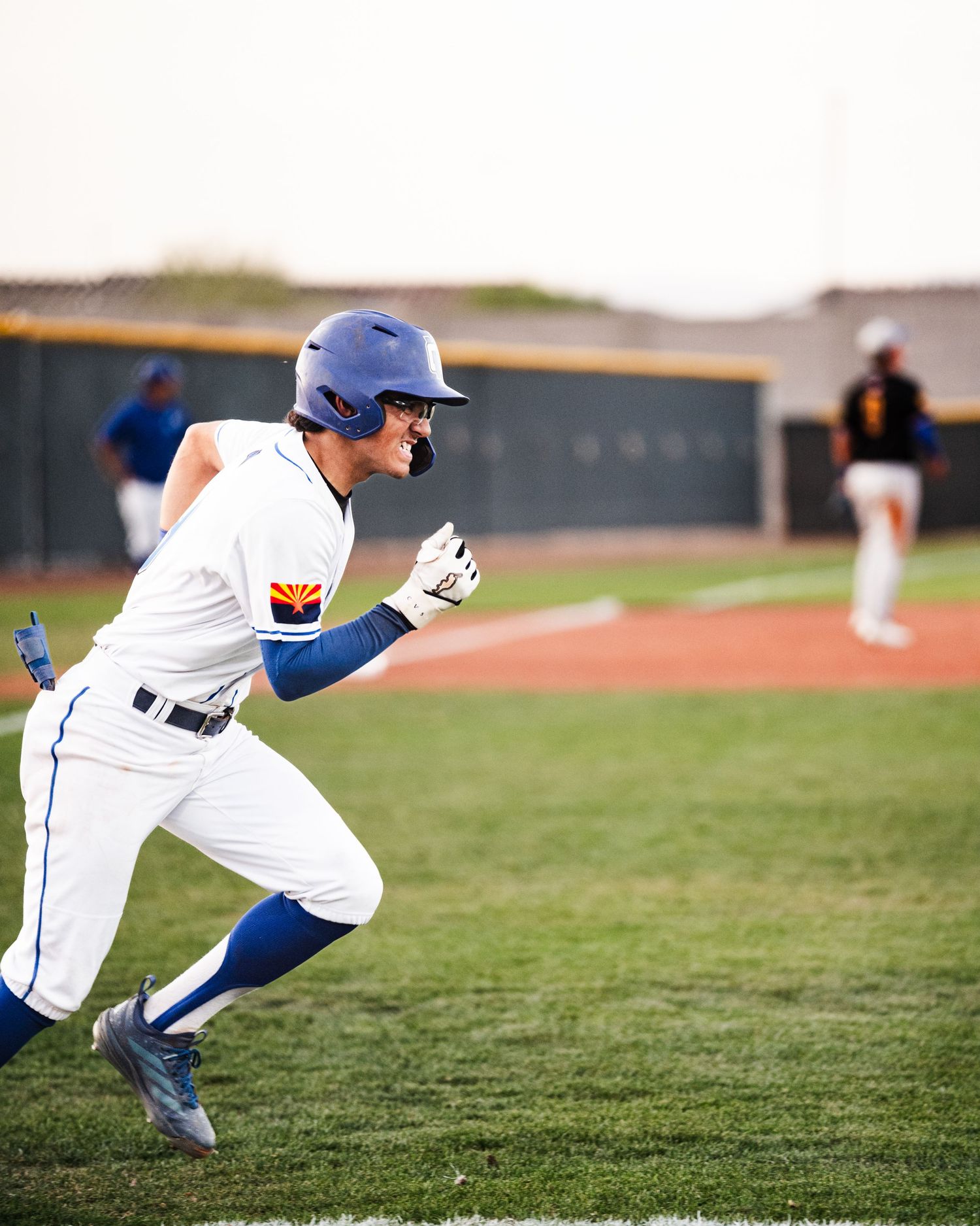 Baseball player in white uniform and blue helmet runs the bases during a game on a sunny day.