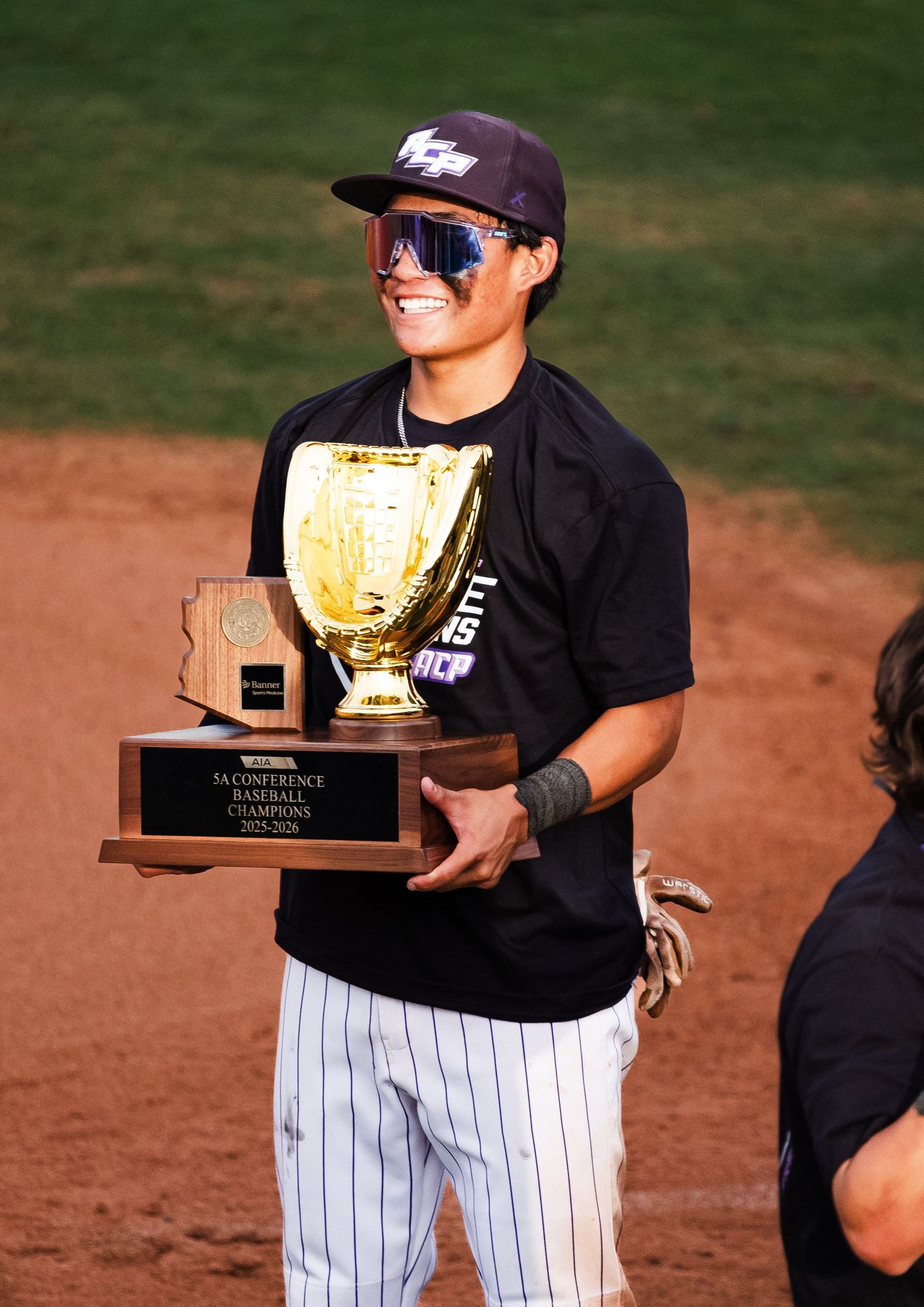 Smiling college baseball player holding gold championship trophy after winning Second District Baseball Championship.
