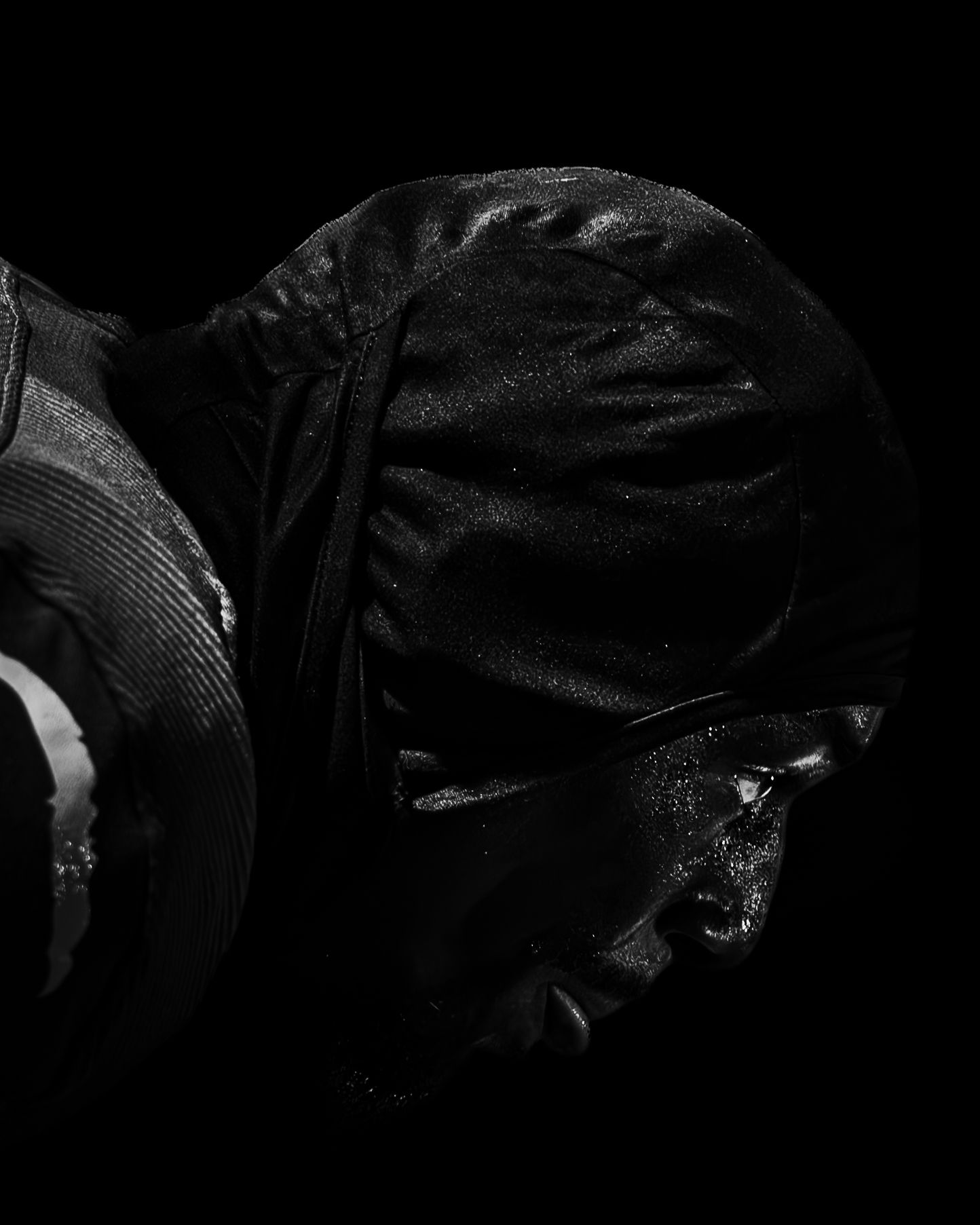 Black and white photo of a cyclist in wet weather gear, helmet glistening with rain droplets against dark background.