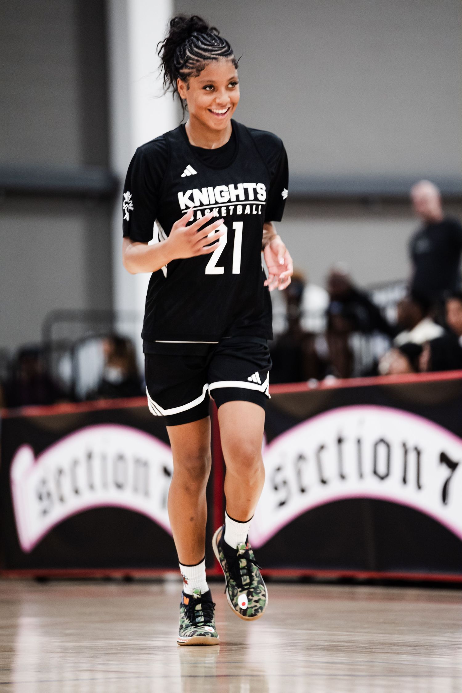 Smiling female basketball player #21 in black Knights Basketball uniform jogs on indoor court.