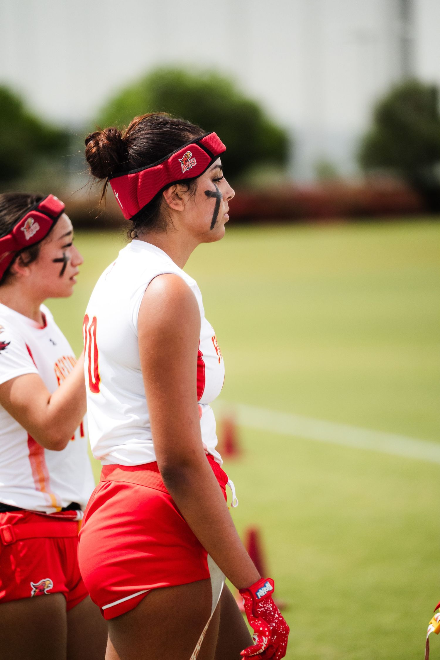 Female flag football players in red and white uniforms with eye black on field during game.