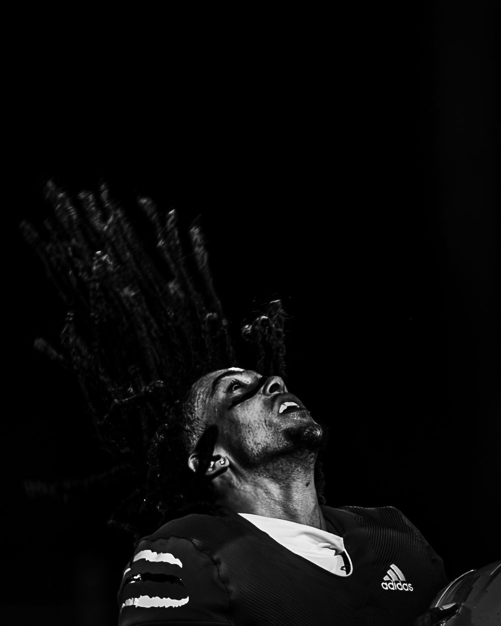 Black and white photo of an athlete with dreadlocks looking up dramatically, wearing an Adidas jersey.